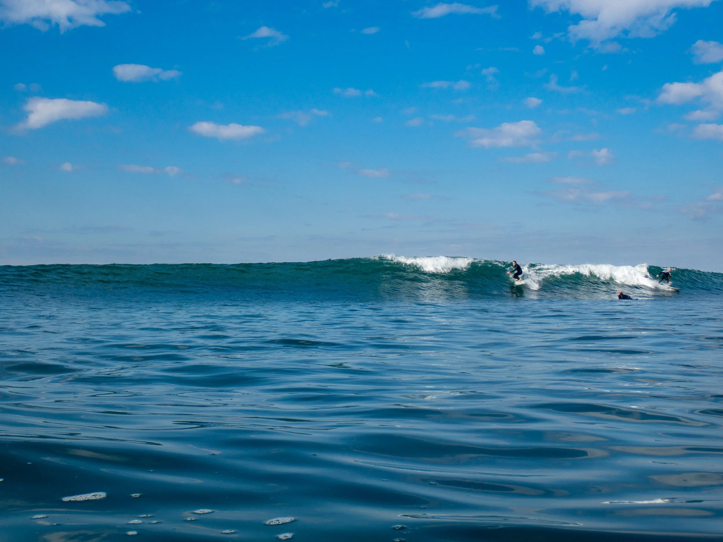 A group of surfers riding and waiting for waves in the ocean under a partly cloudy sky.