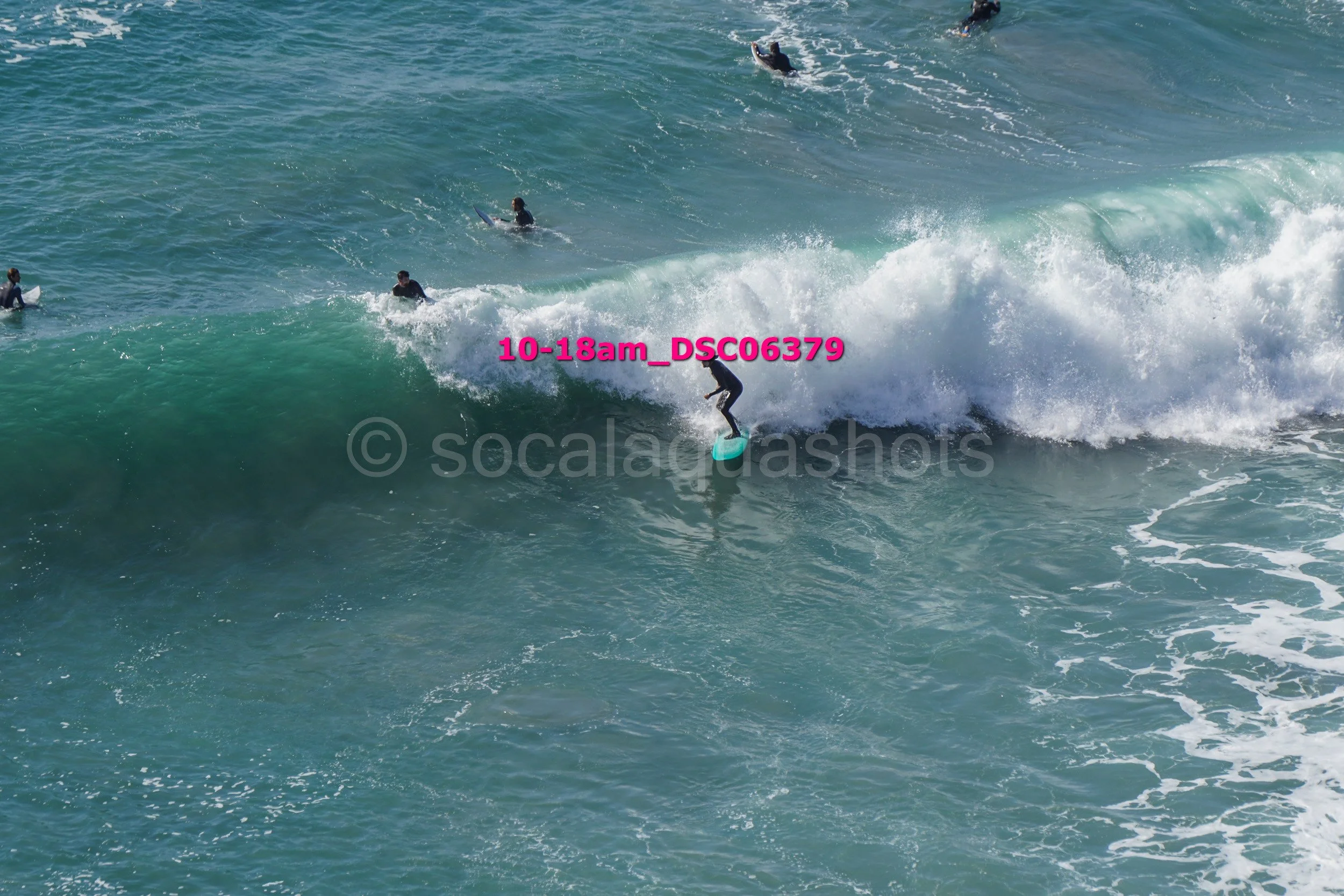 A person surfing on a large blue wave with several other surfers in the water nearby.