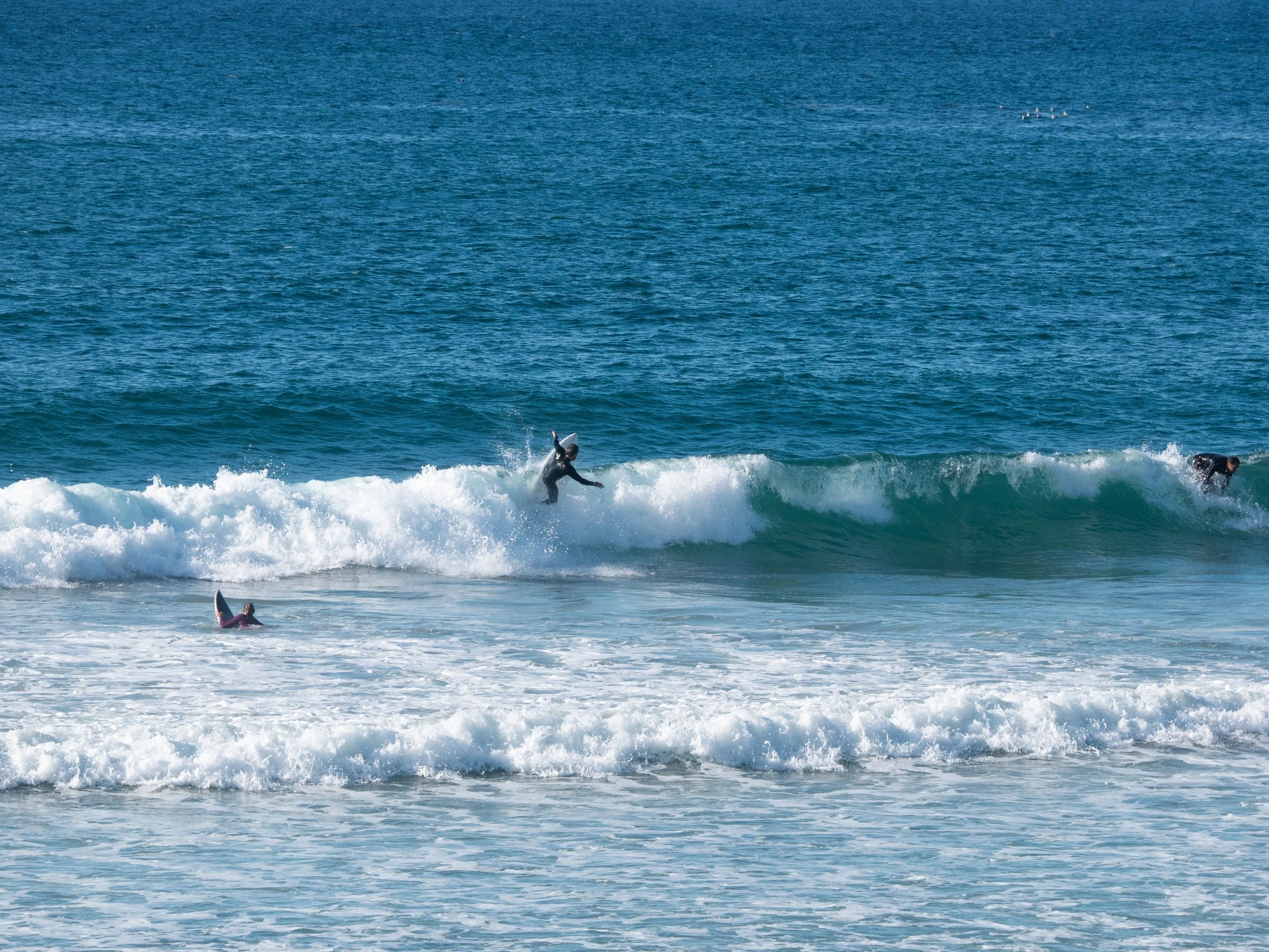 People surfing on ocean waves near the shore, with one person riding a wave and another in the water nearby.