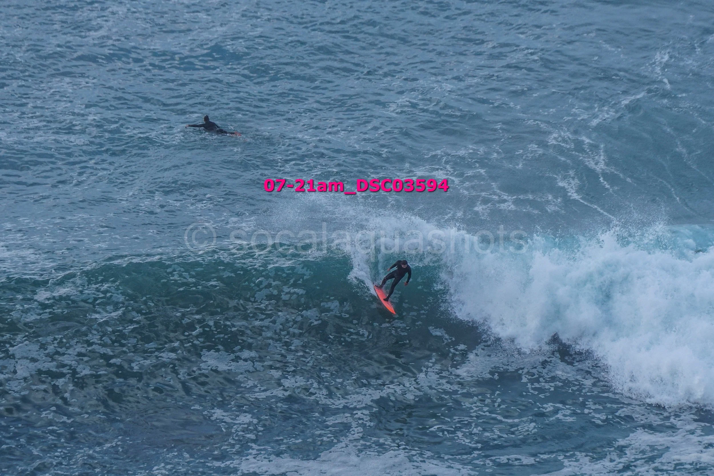 Surfer riding a wave with a person swimming in the water nearby.