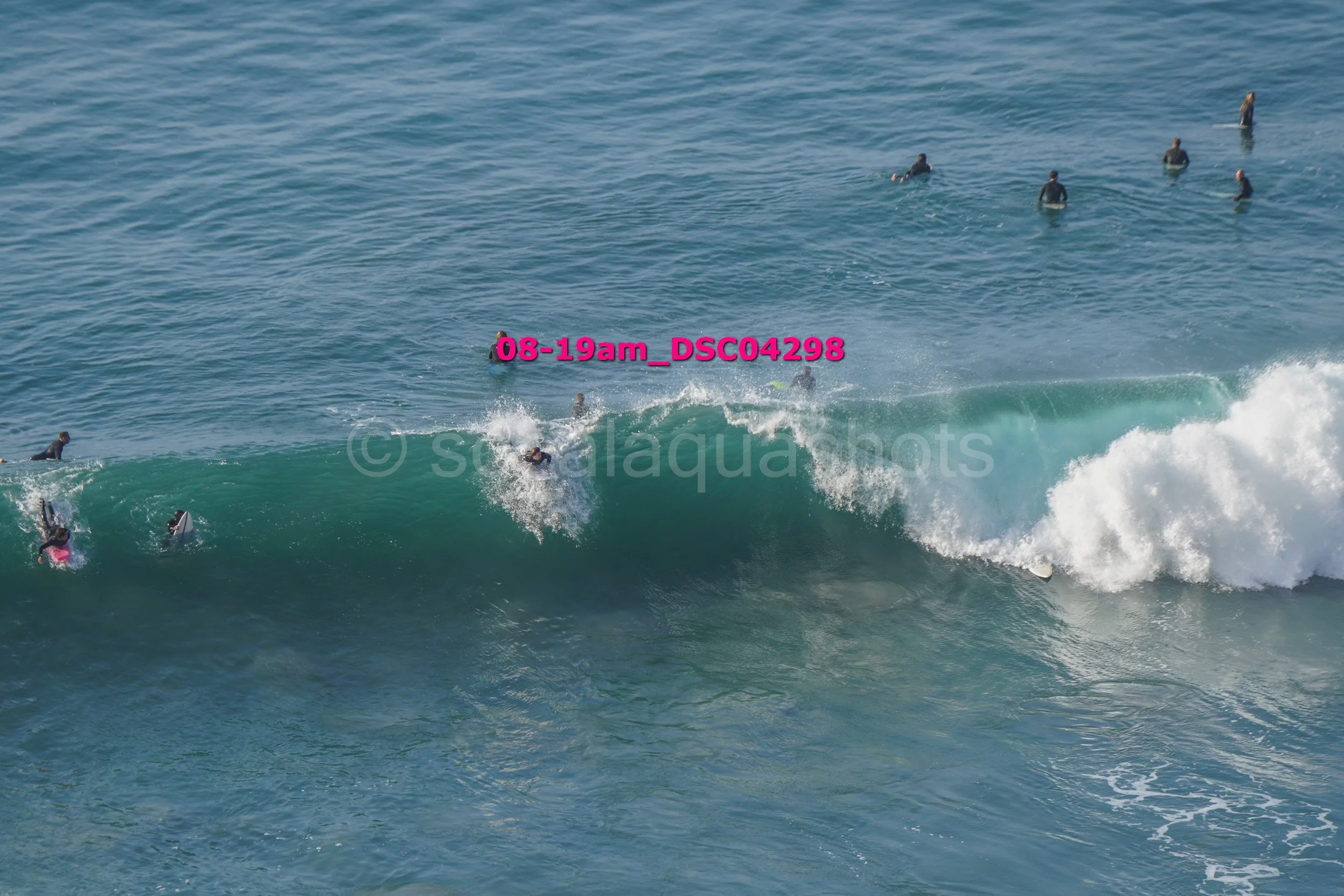 Several surfers in wetsuits and surfboards riding and waiting for waves in the ocean.