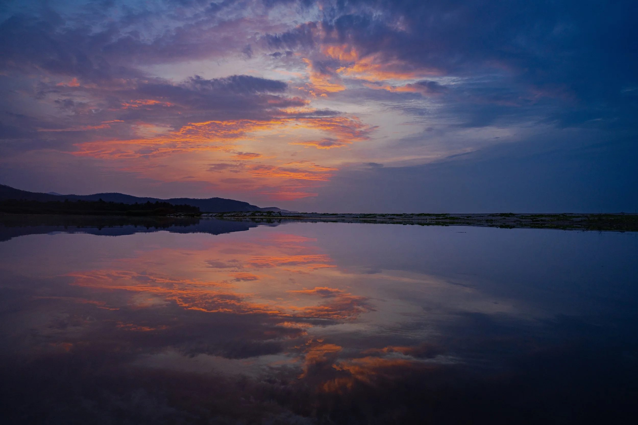 Sunset over mountains reflected in a body of water with clouds in the sky.