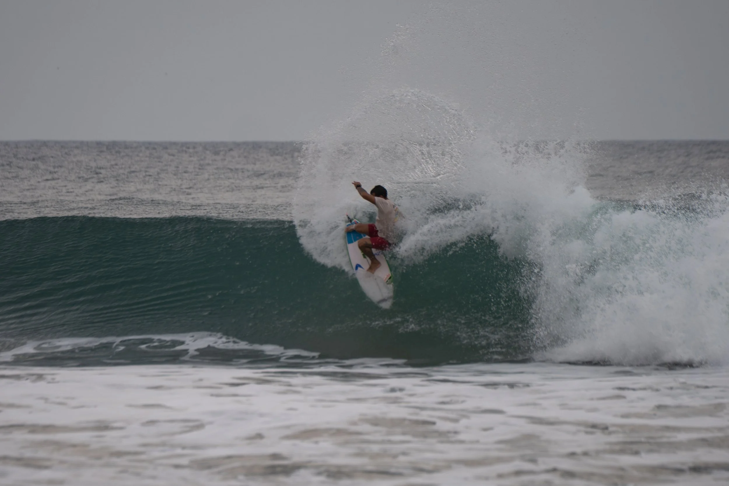 A person surfing on a wave in the ocean during daylight with gray sky.