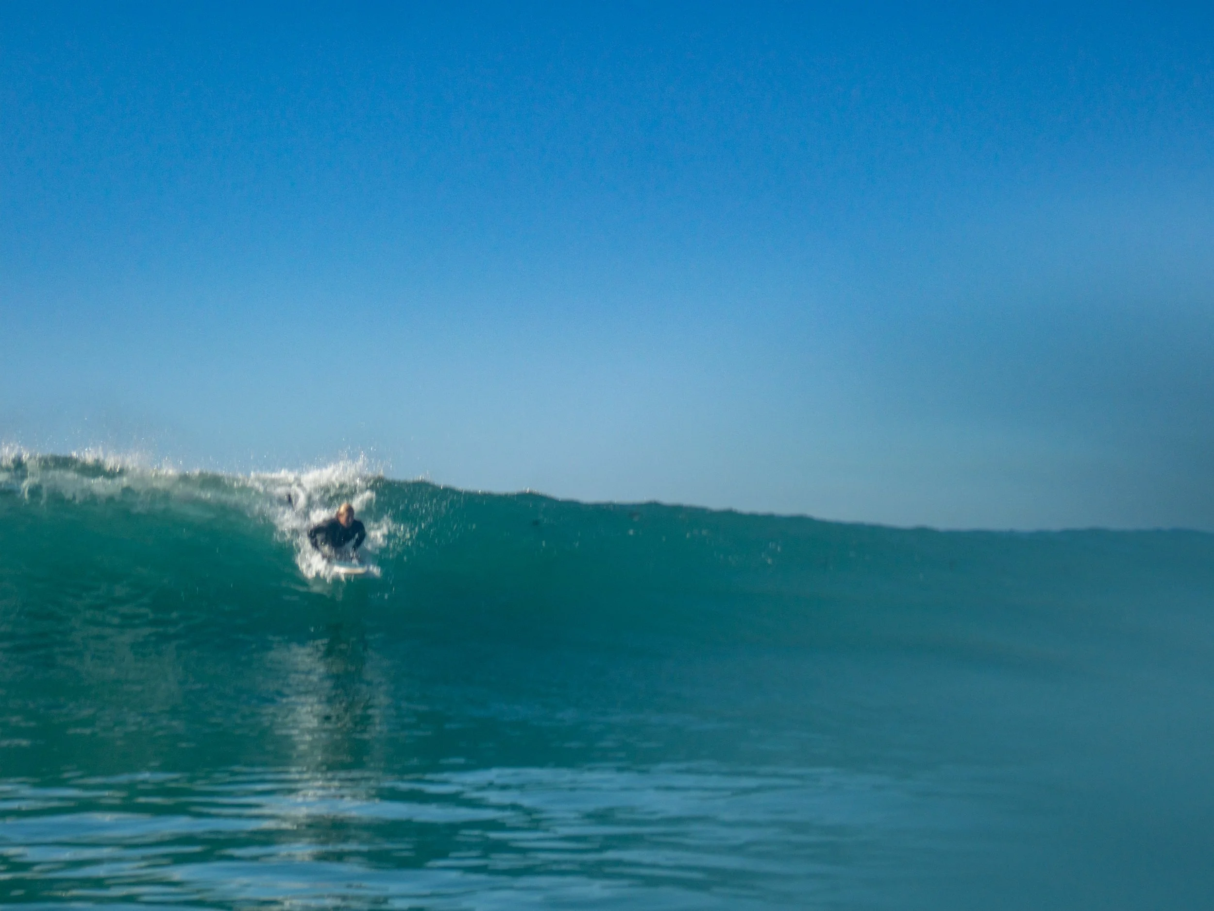 A surfer riding a large wave in the ocean on a clear day with a blue sky.