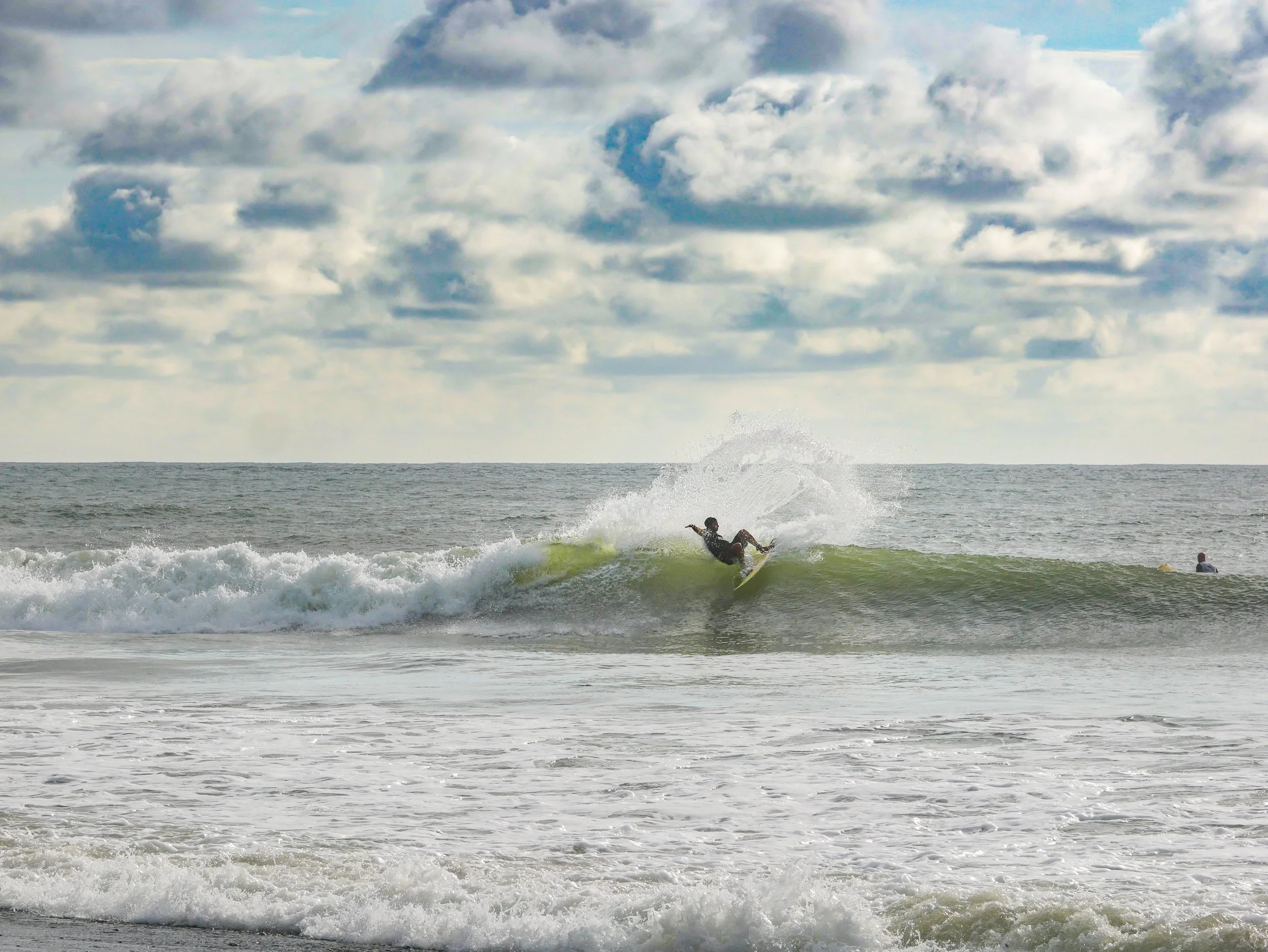 Surfer riding a wave in the ocean with cloudy sky