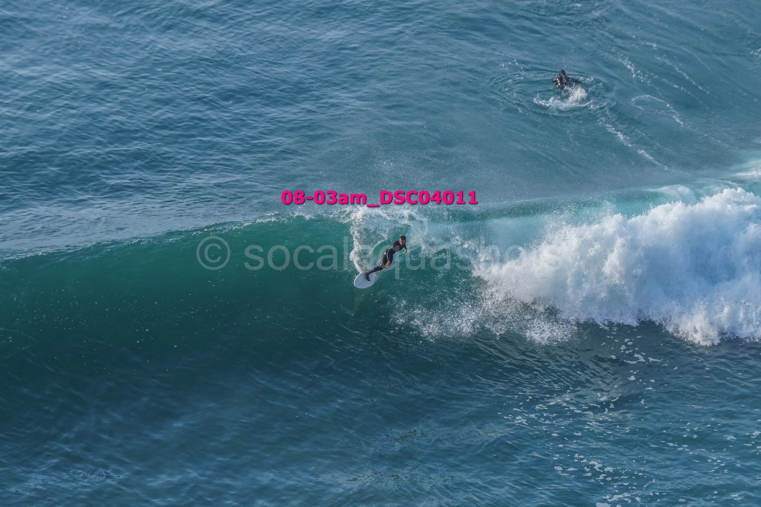 A person surfing on a wave in the ocean, with another surfer visible in the distance.