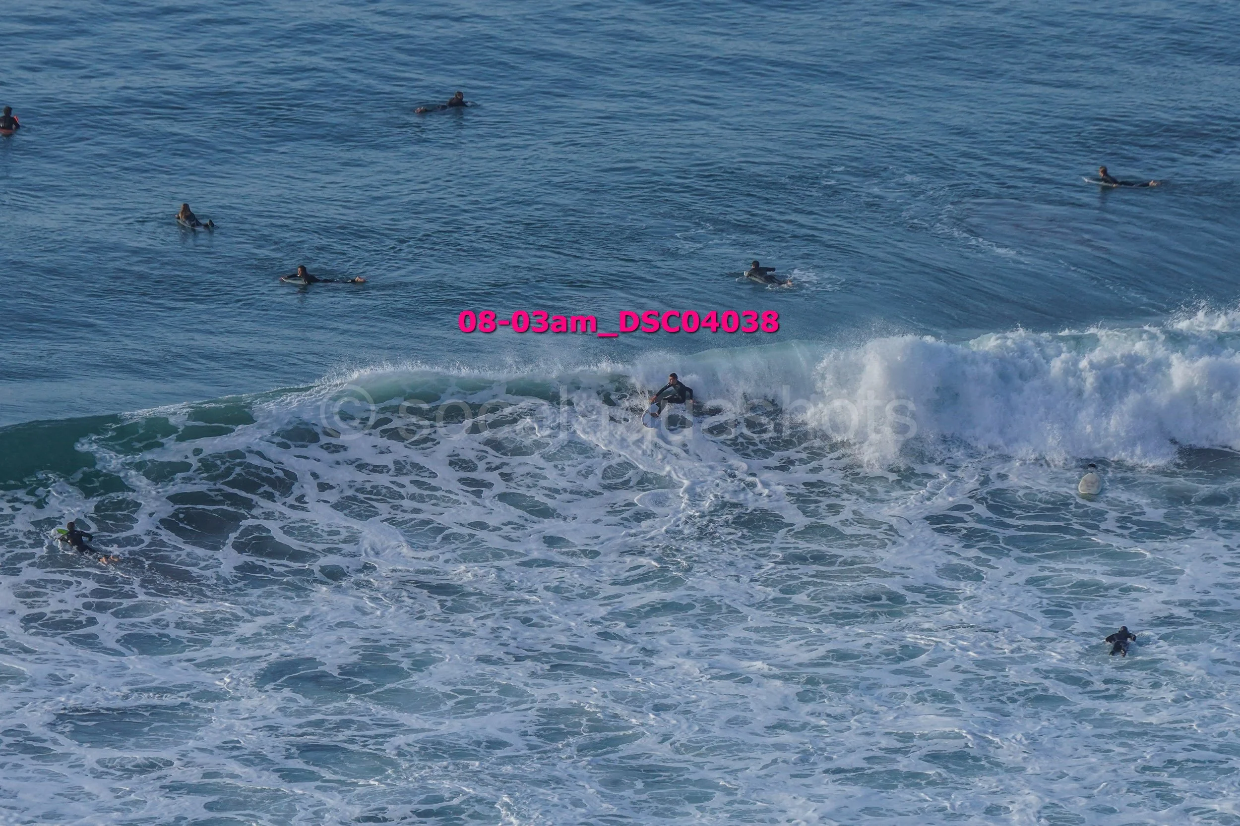 Surfers in the ocean with one surfer riding a wave and others waiting or swimming in the water.
