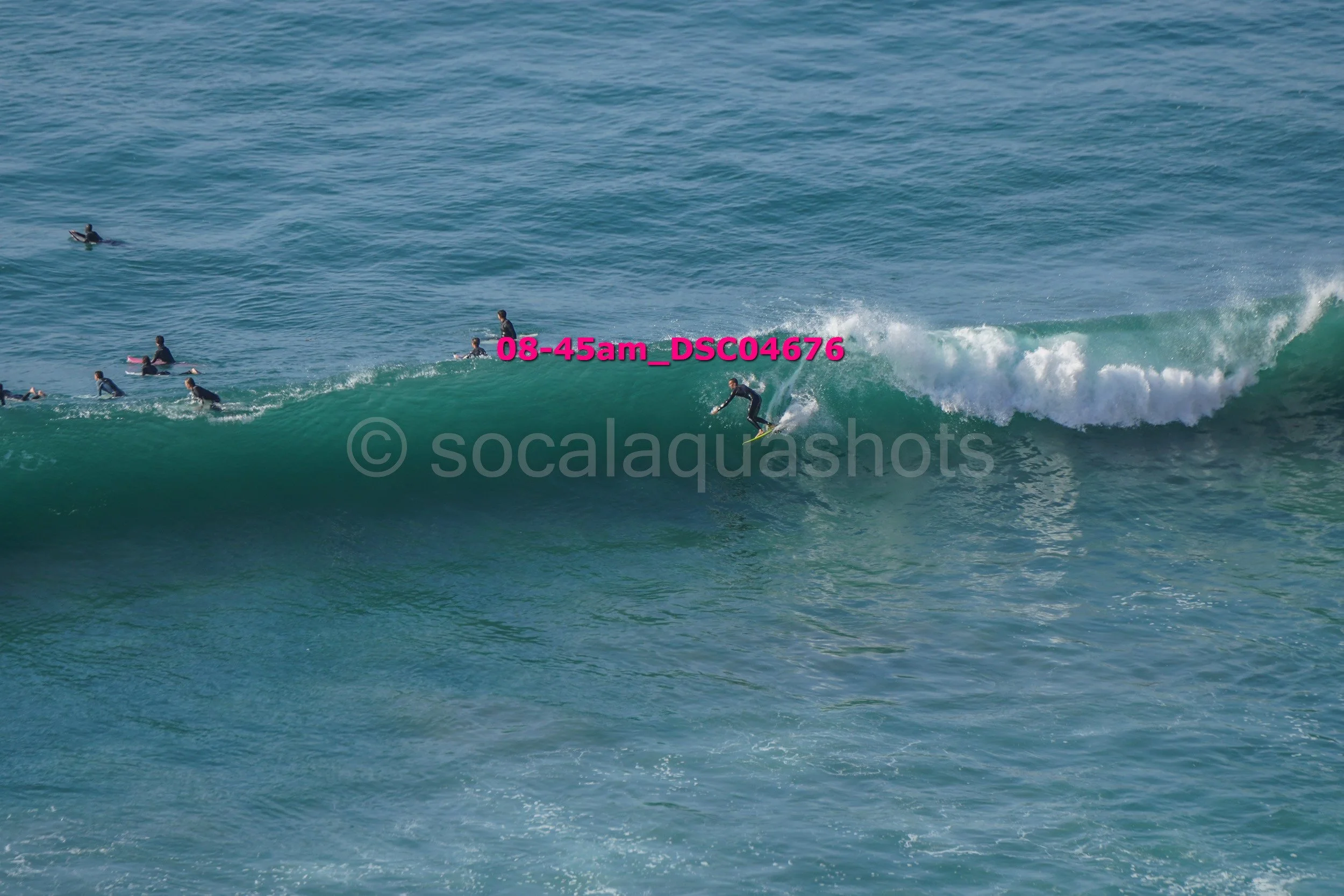 A surfer riding a wave with several other surfers in the water nearby.