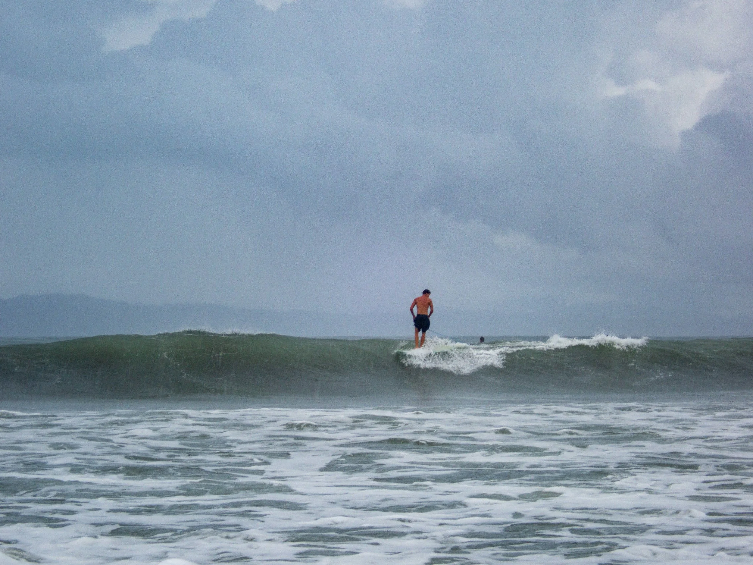 A person surfing on a wave under a cloudy sky.