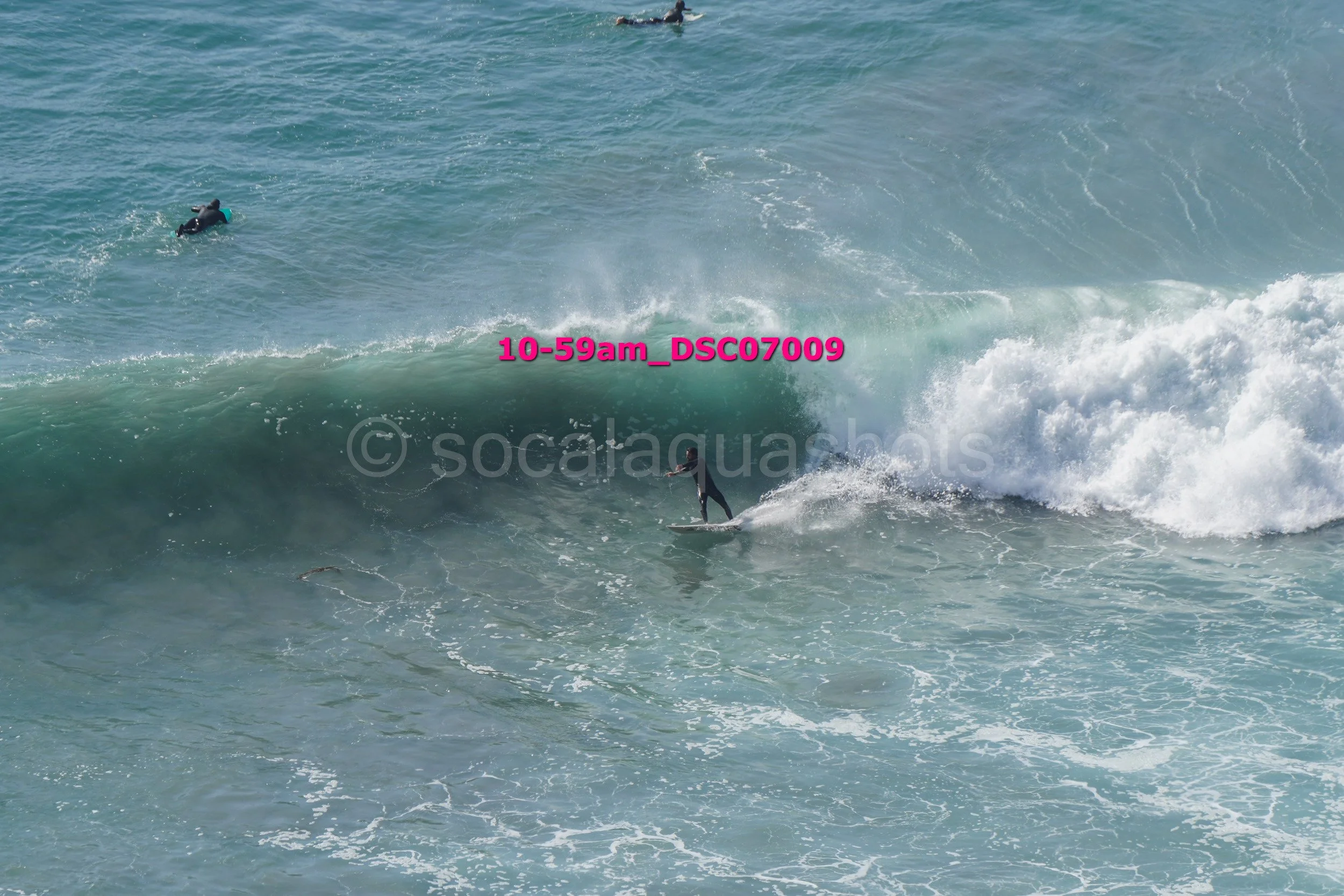 A surfer riding a wave with two other surfers in the water nearby.