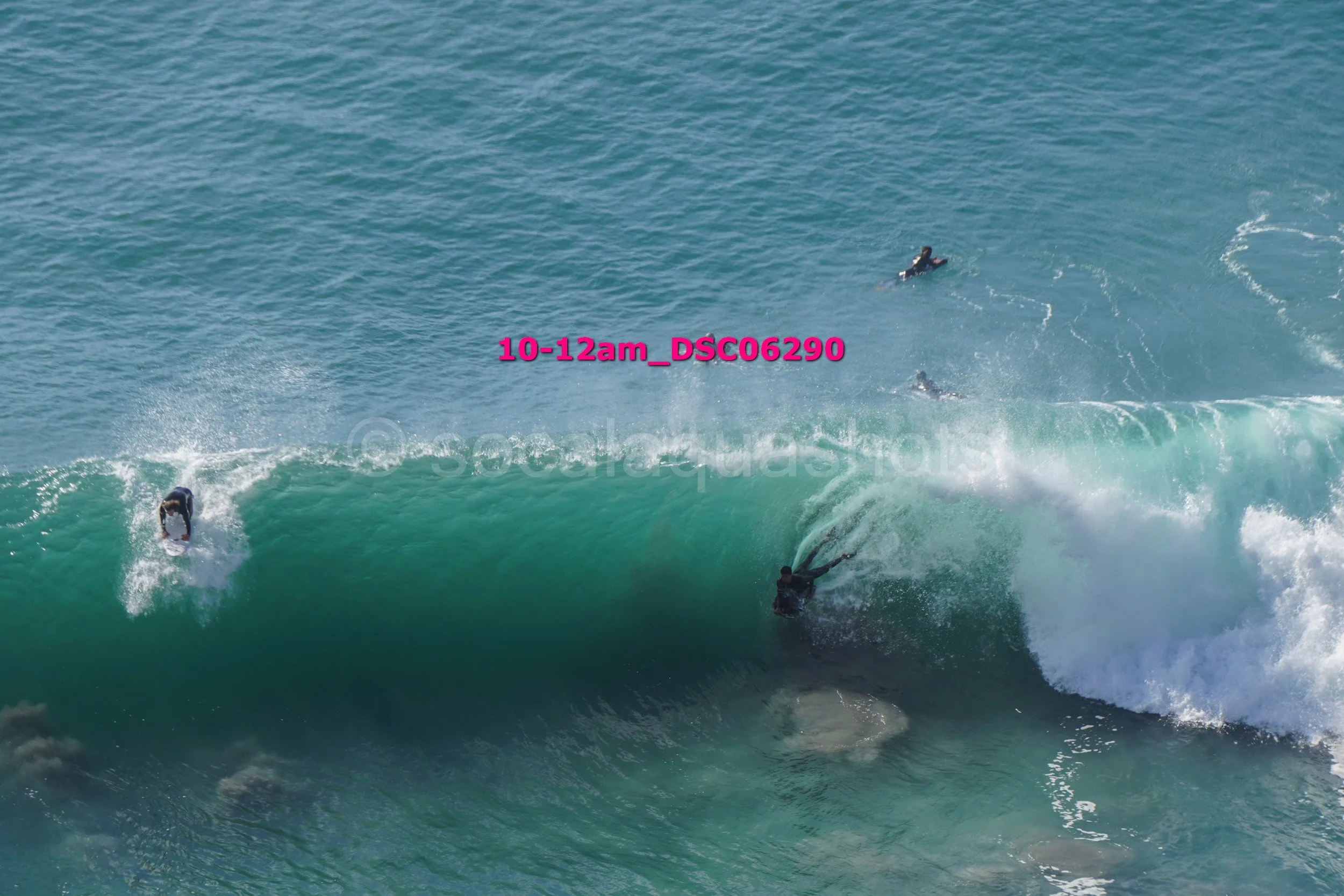 A person surfing on a large wave with two other surfers in the water nearby.