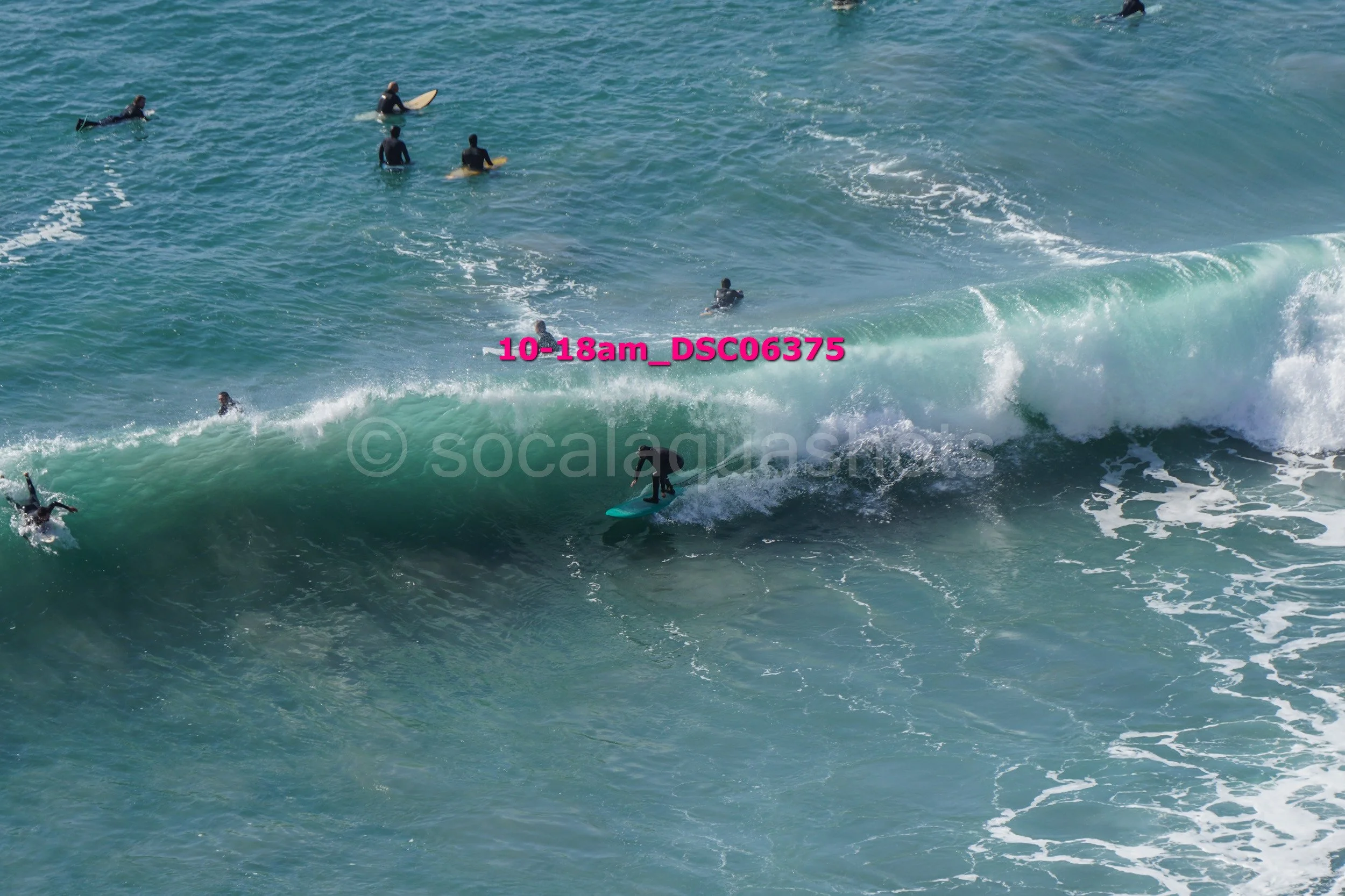 Surfers riding and waiting for waves in the ocean with multiple people on surfboards and in the water.