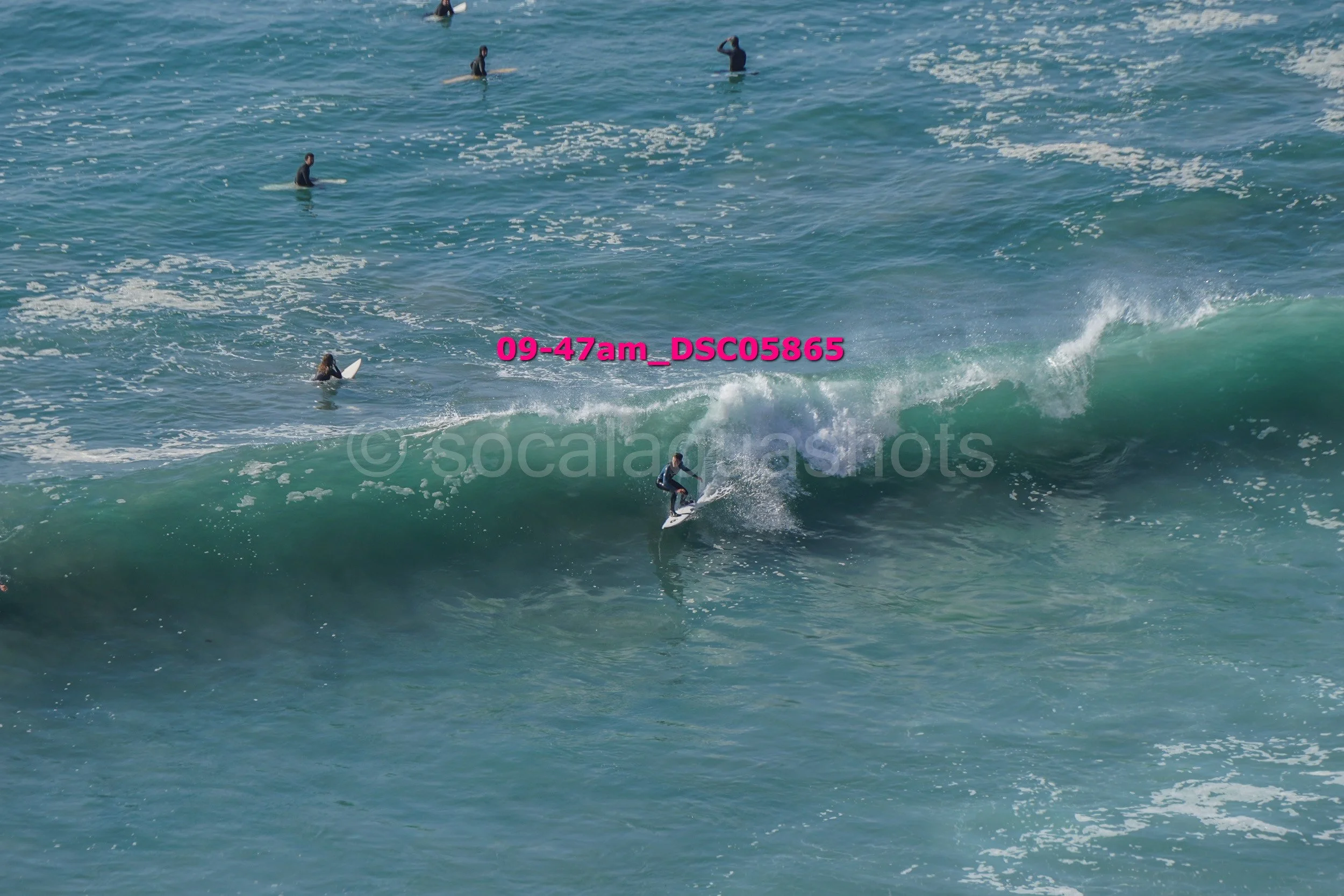 Surfer riding a wave with several surfers in the background in the ocean.
