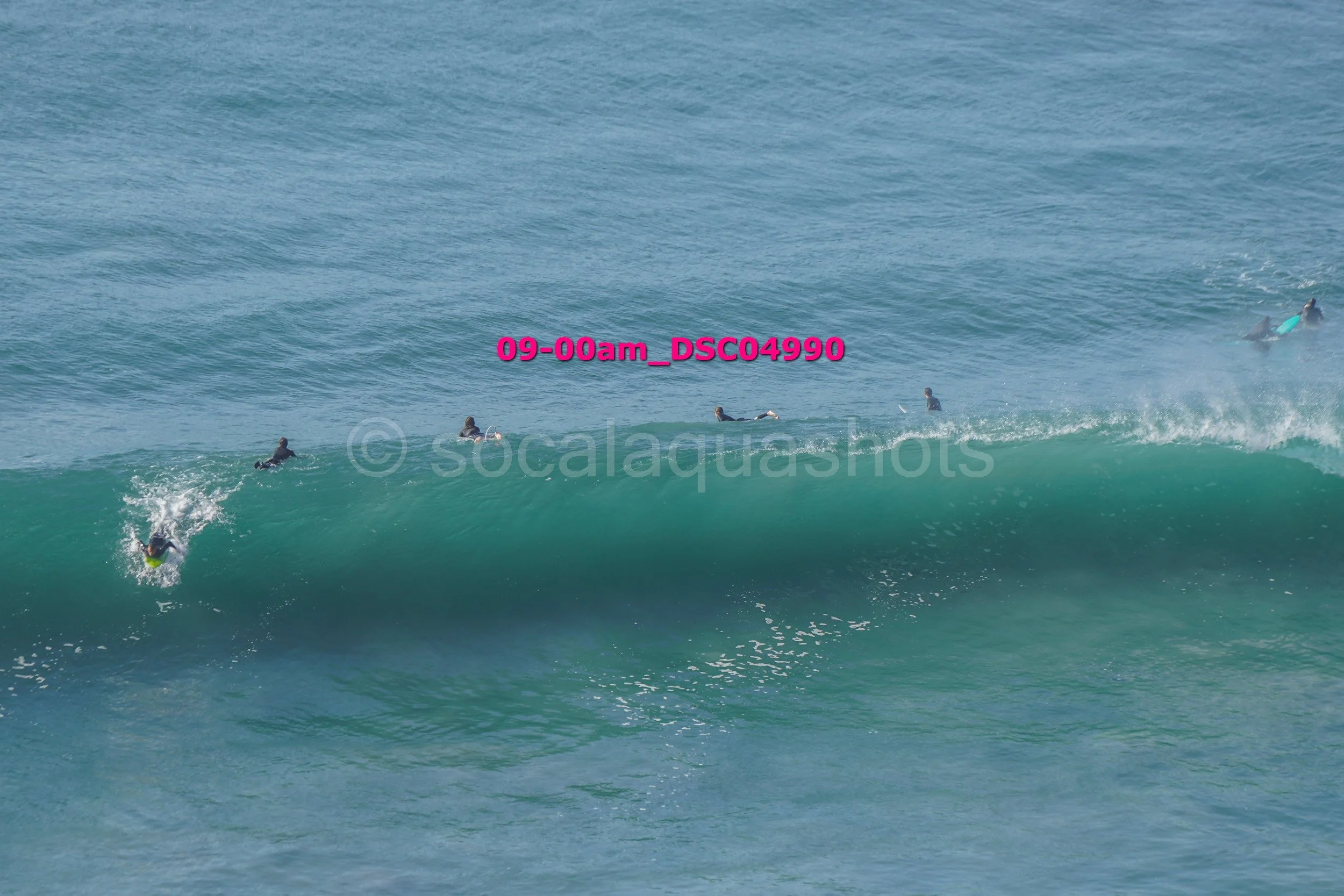 Surfers paddling and riding waves in the ocean with one surfer in a green surfboard on a large wave.