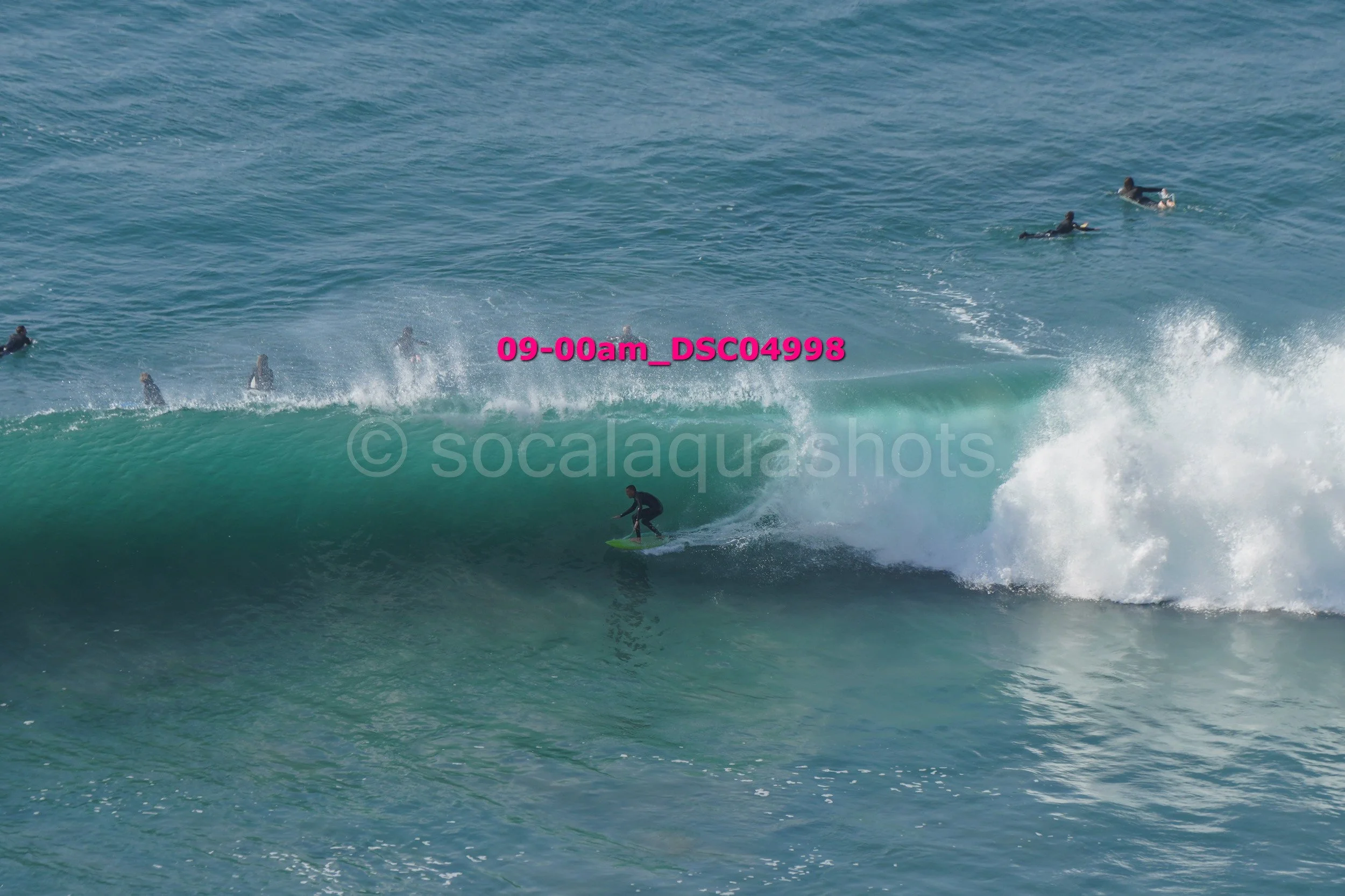 A surfer riding a wave in the ocean with several other surfers in the water around them.