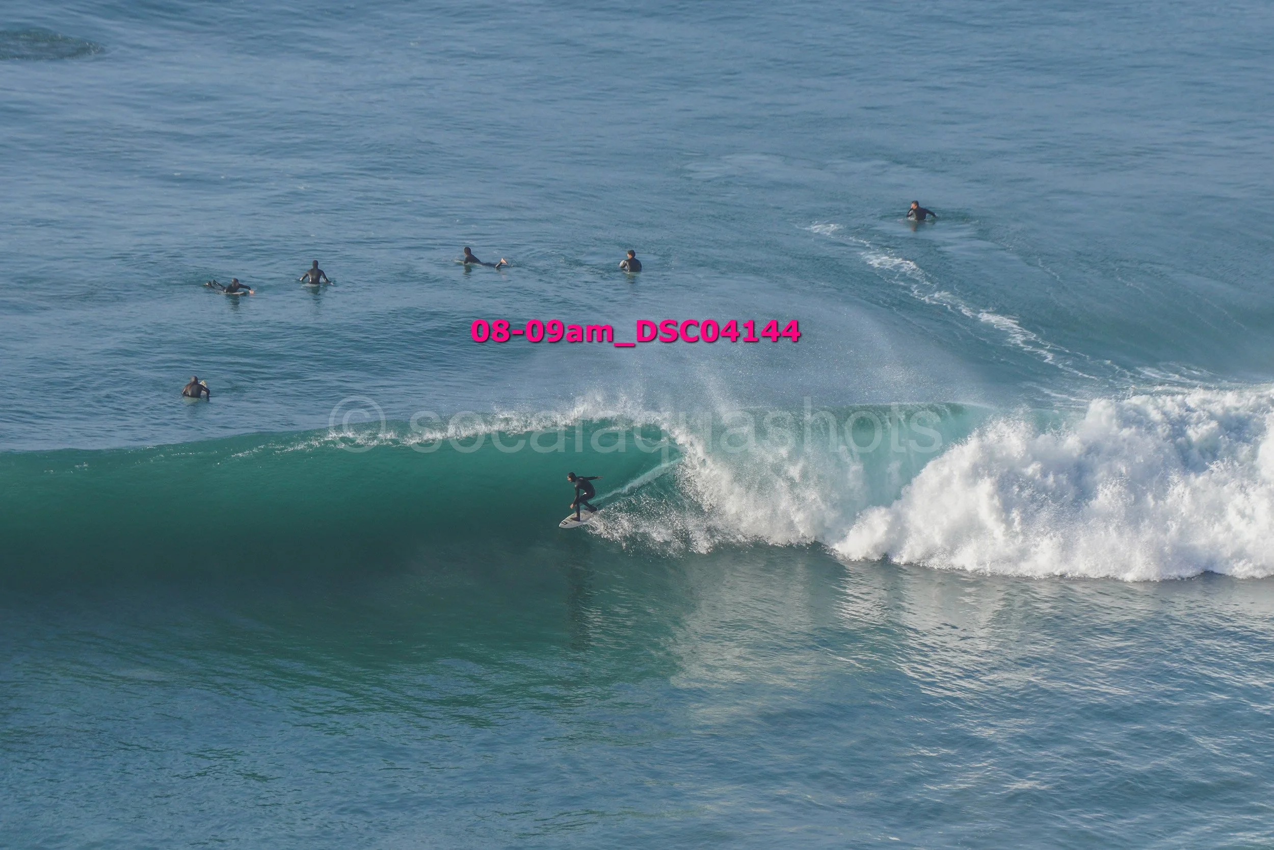 A person surfing on a wave with several people in the water watching.