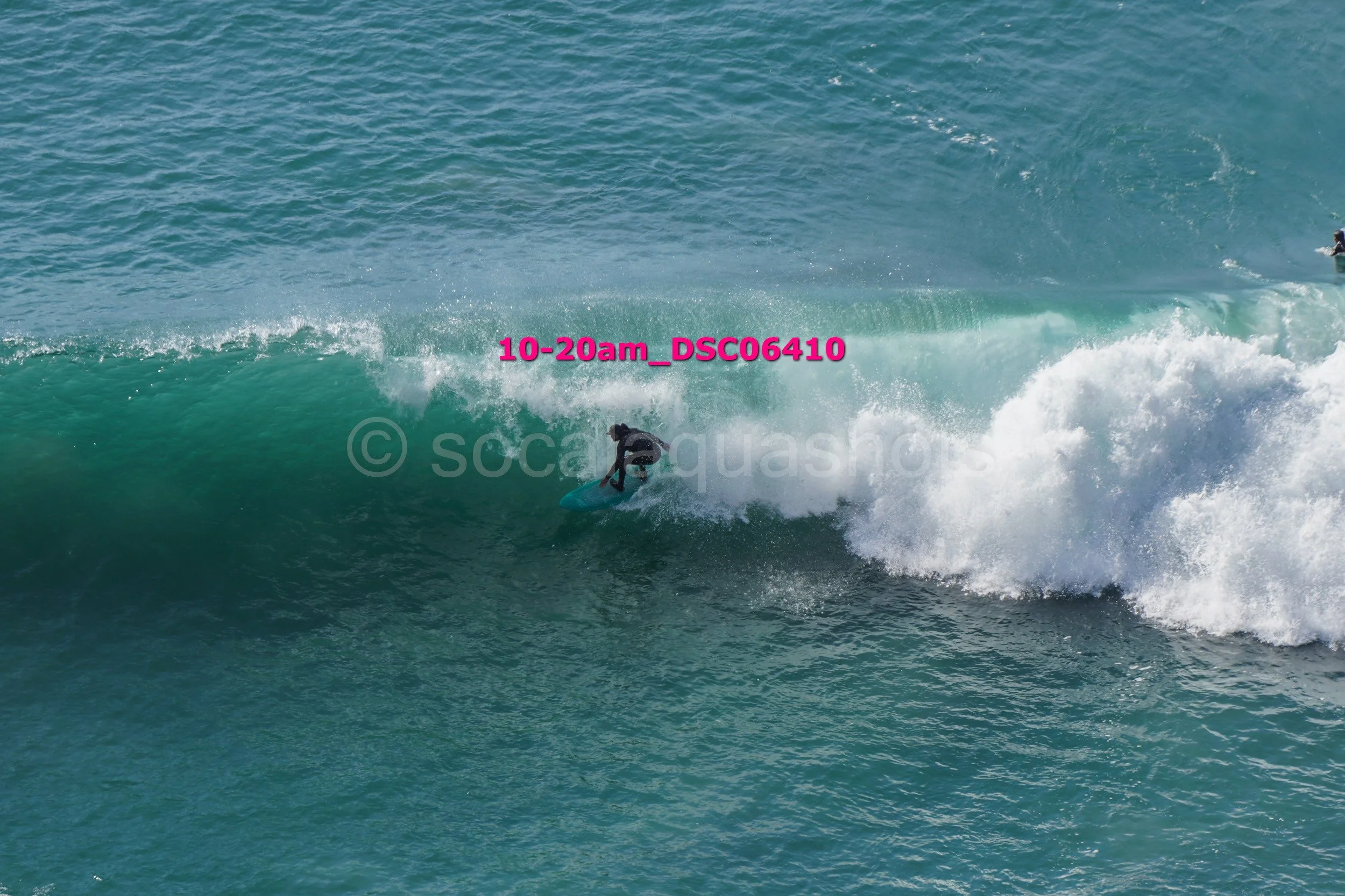 A surfer riding inside the wave on the ocean, with visible water spray and a cloudy sky.