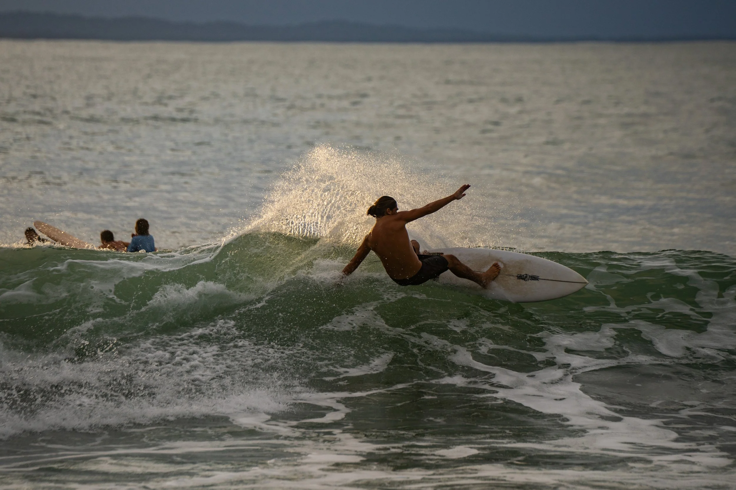 A man surfing on a wave with three children in the background in the ocean.