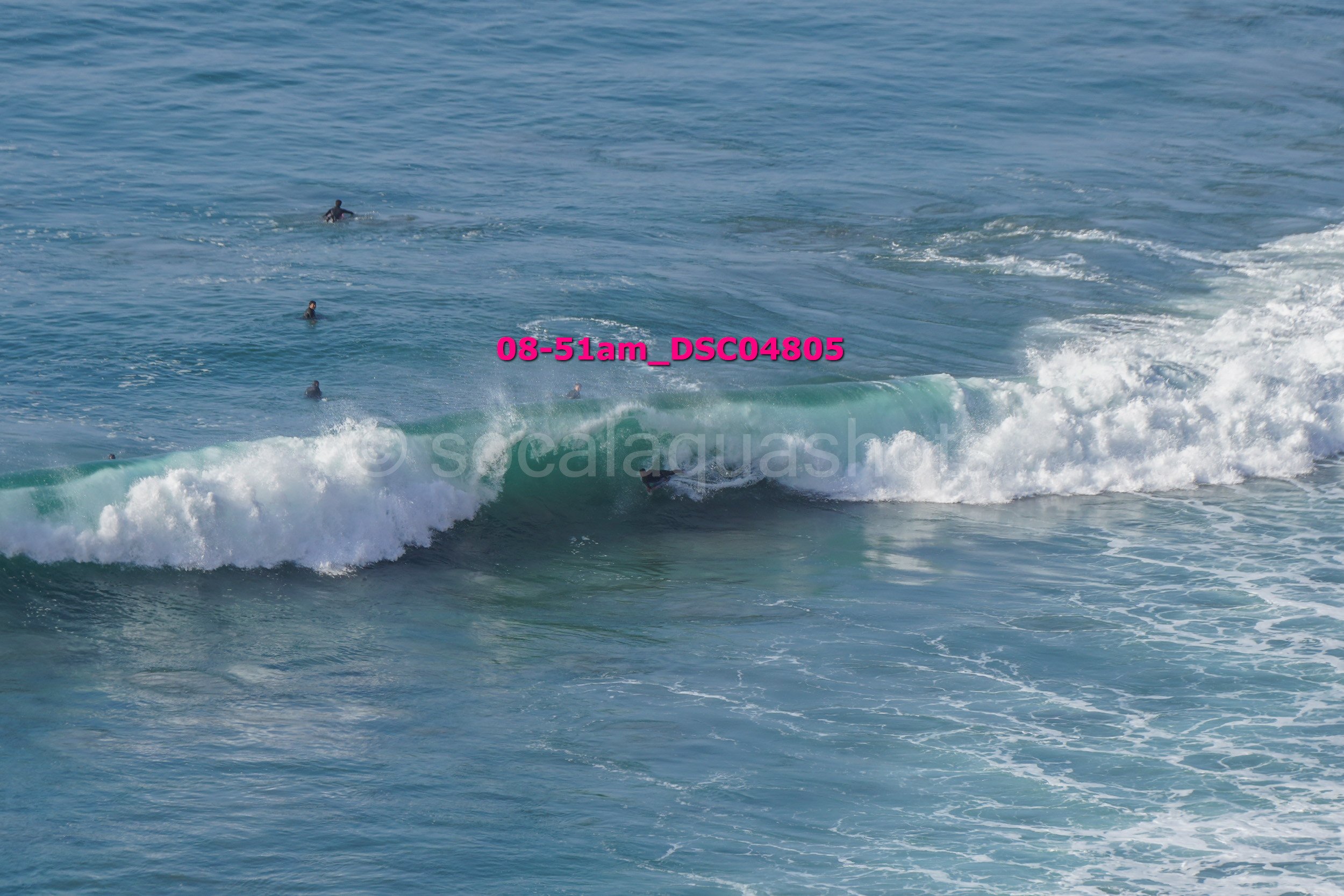 People surfing in the ocean with a wave breaking and a surfer riding it.