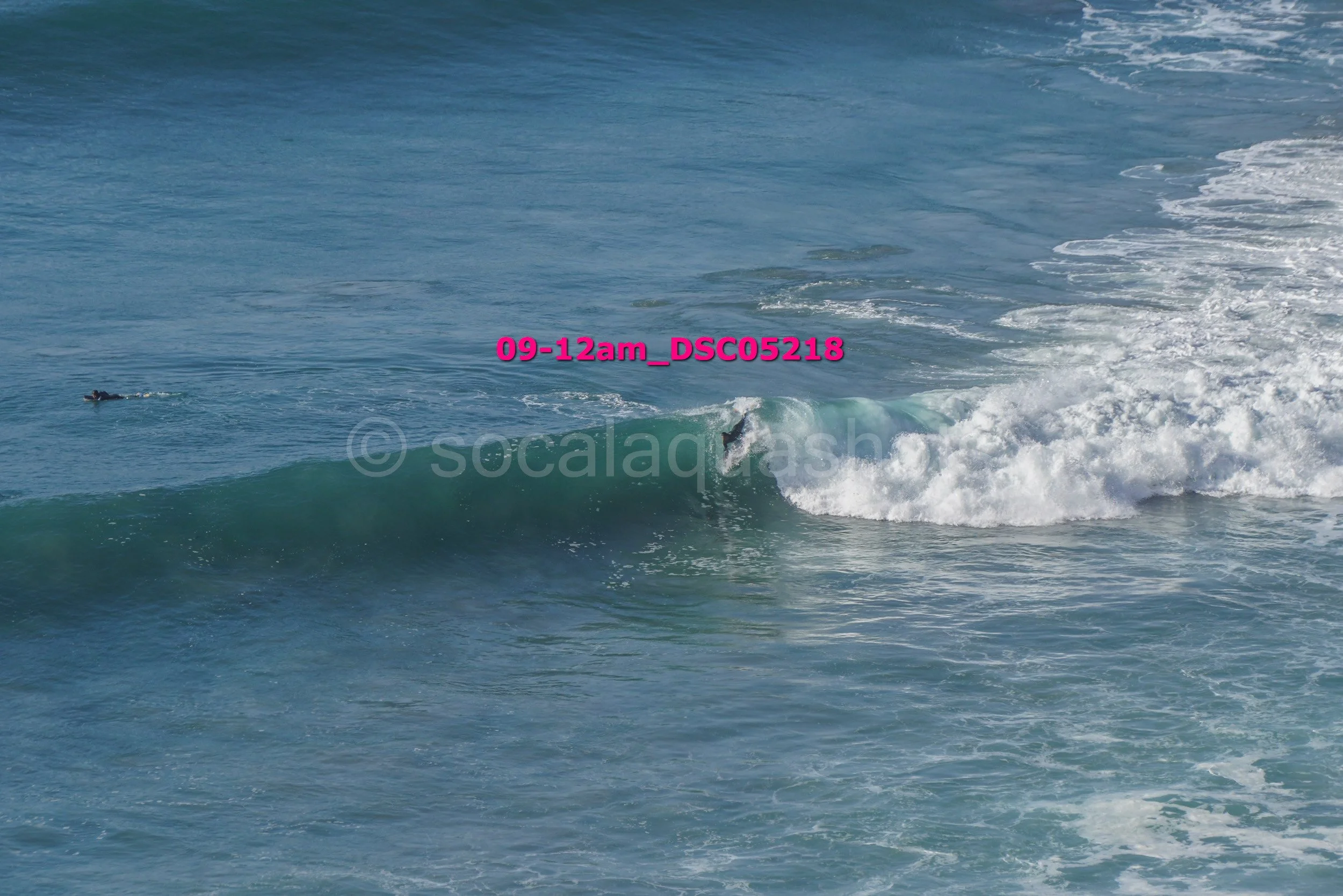A person surfing a wave in the ocean, with another person swimming nearby.