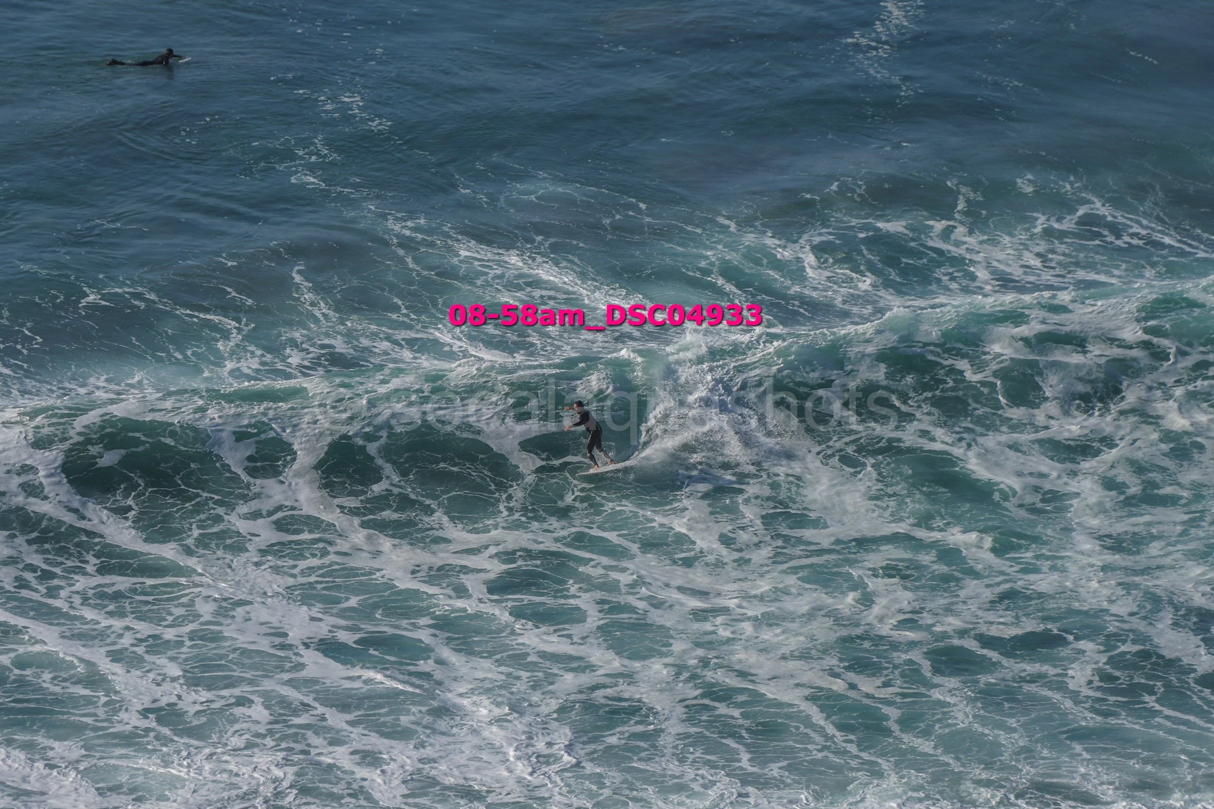 A person surfing on the ocean waves with two other surfers visible in the distance.