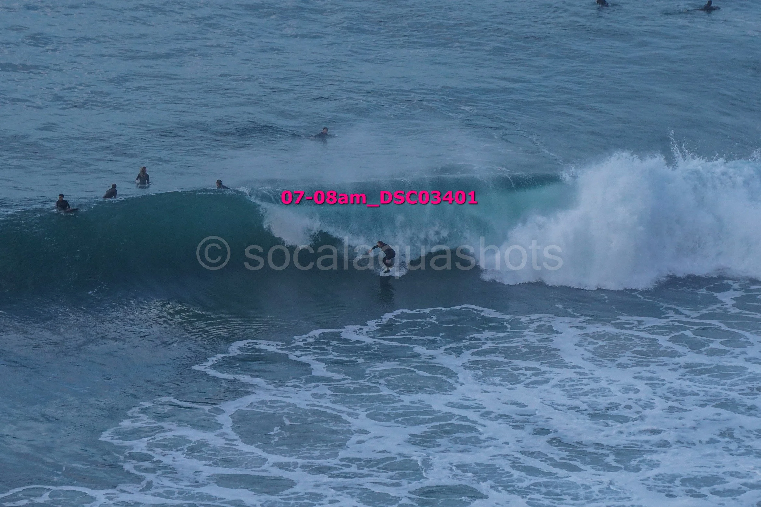 Surfer riding a wave with several people in the water nearby.