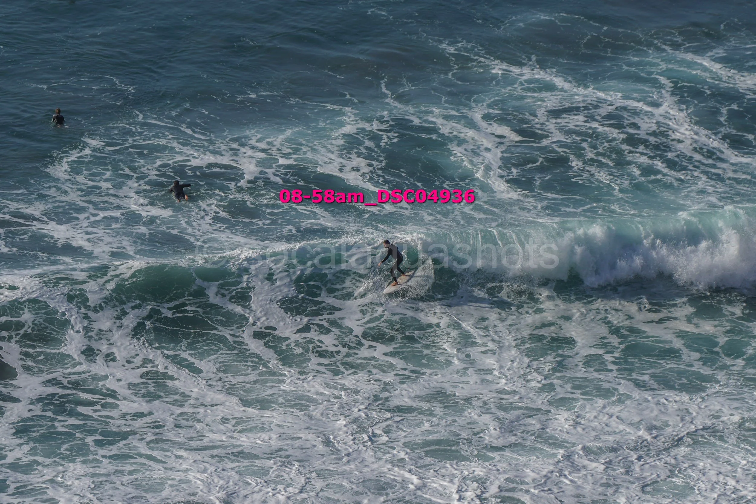 Surfer riding a wave with two other surfers in the water nearby.
