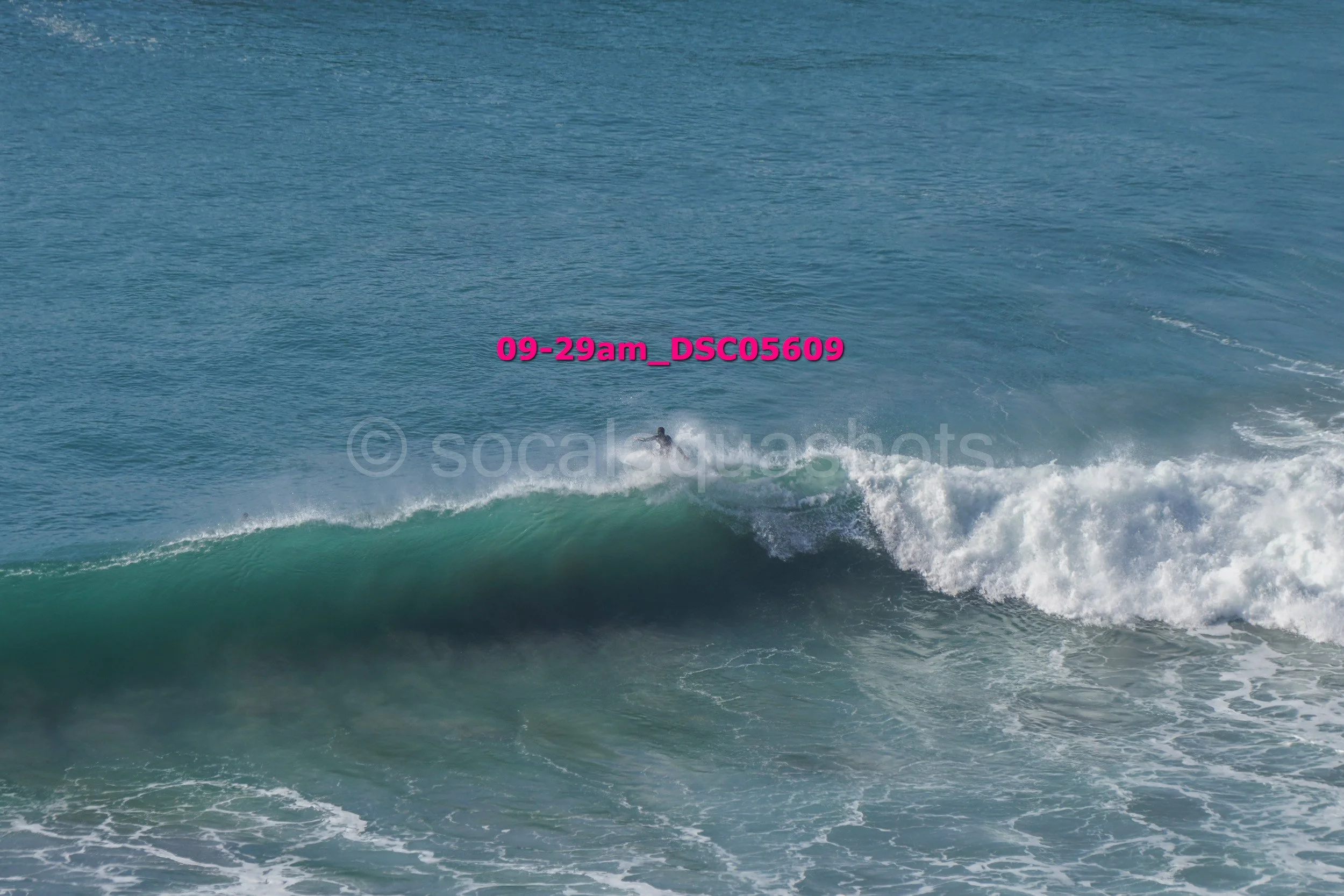 A surfer riding a wave in the ocean with a clear sky in the background.
