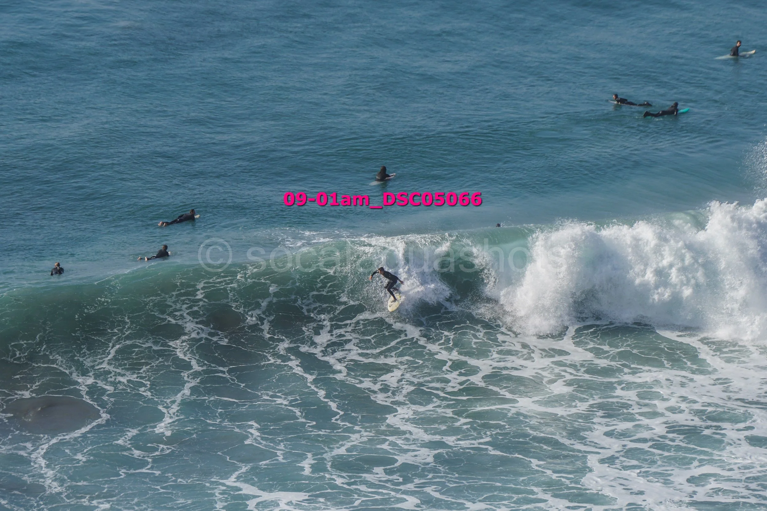 A surfer riding a wave while several people are swimming and surfing in the ocean nearby.