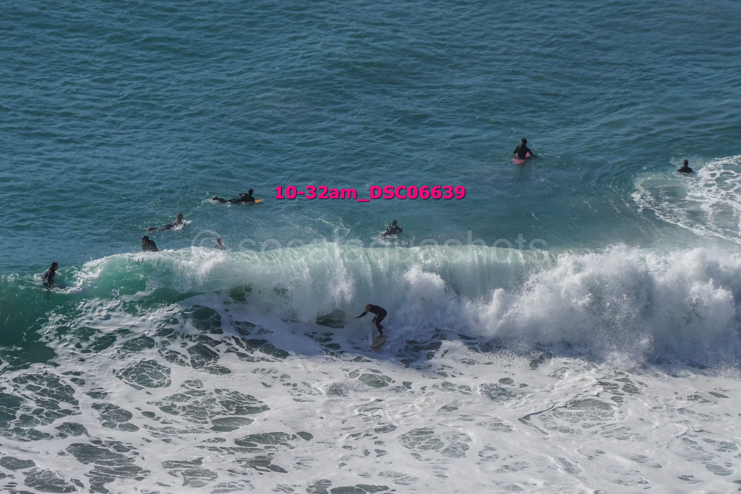 Surfer riding a wave with several people swimming in the ocean nearby.