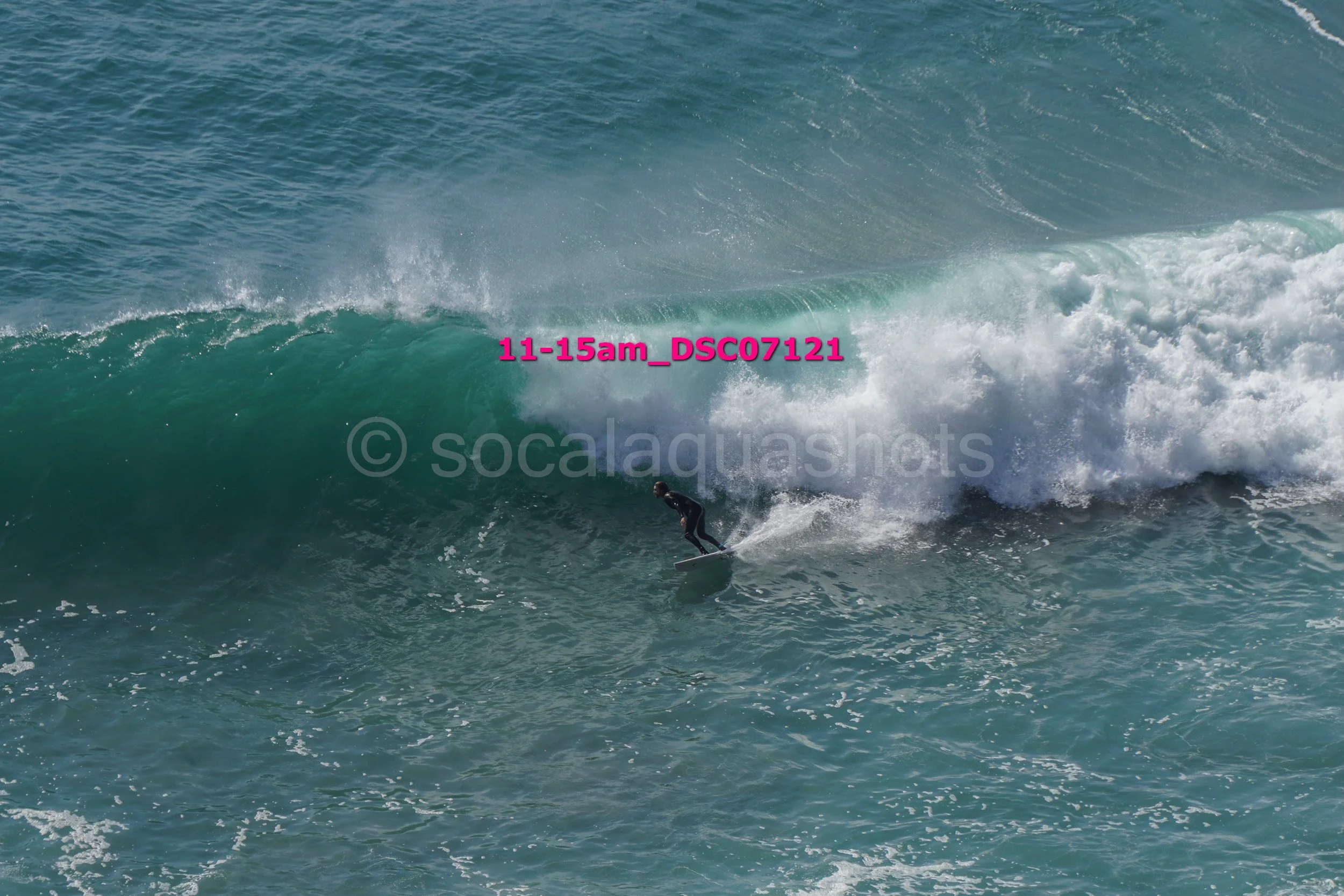 A surfer in a black wetsuit riding a large blue wave in the ocean.