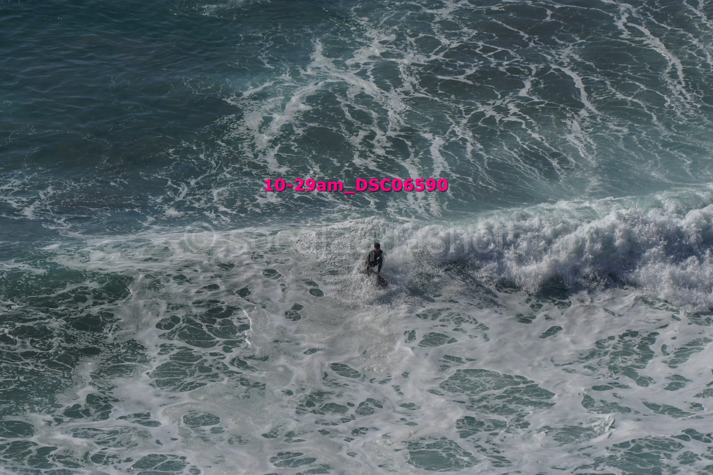A person surfing on the ocean waves with surfboard in the water. Water appears rough with white foam and waves.
