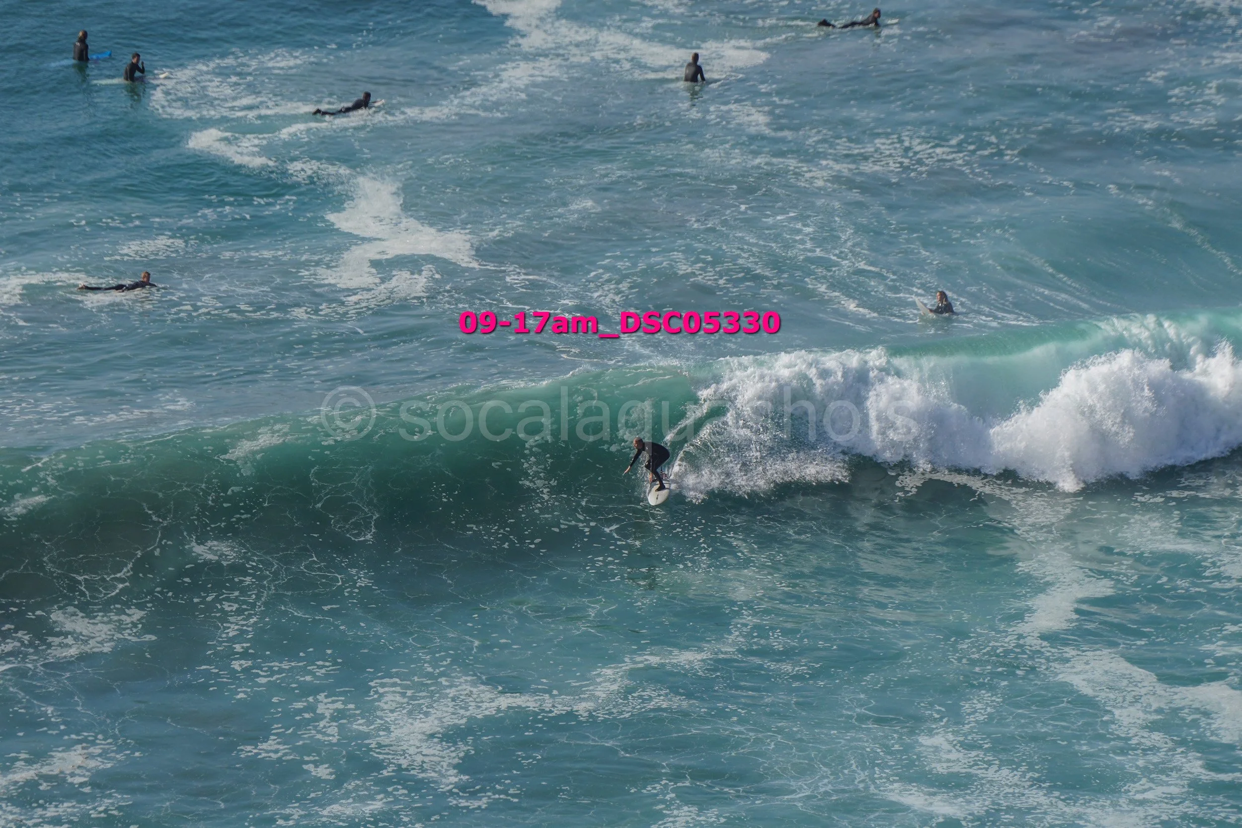 A group of surfers in wetsuits surfing and floating in the ocean with waves