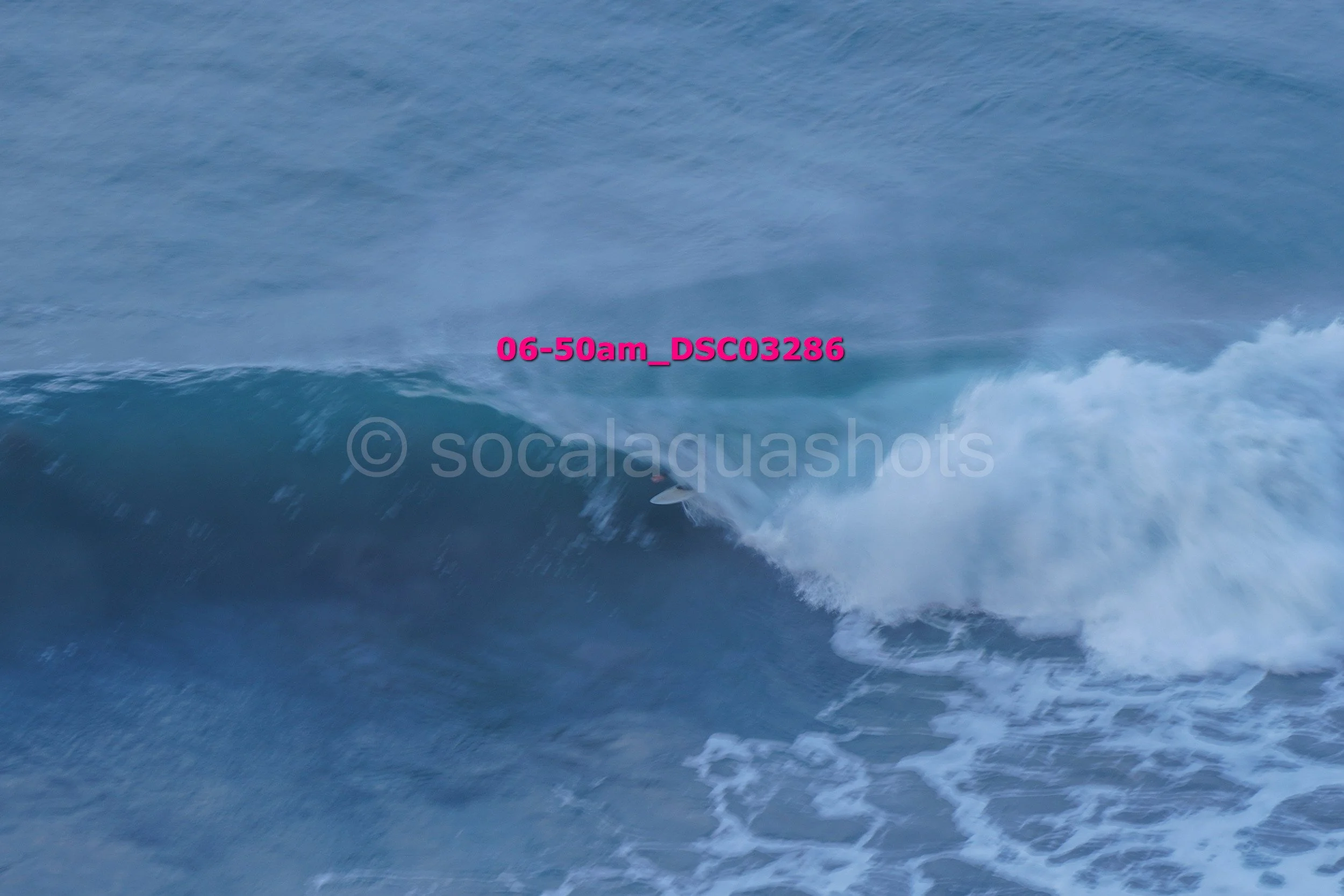 A person surfing on a large wave in the ocean with spray and white foam.
