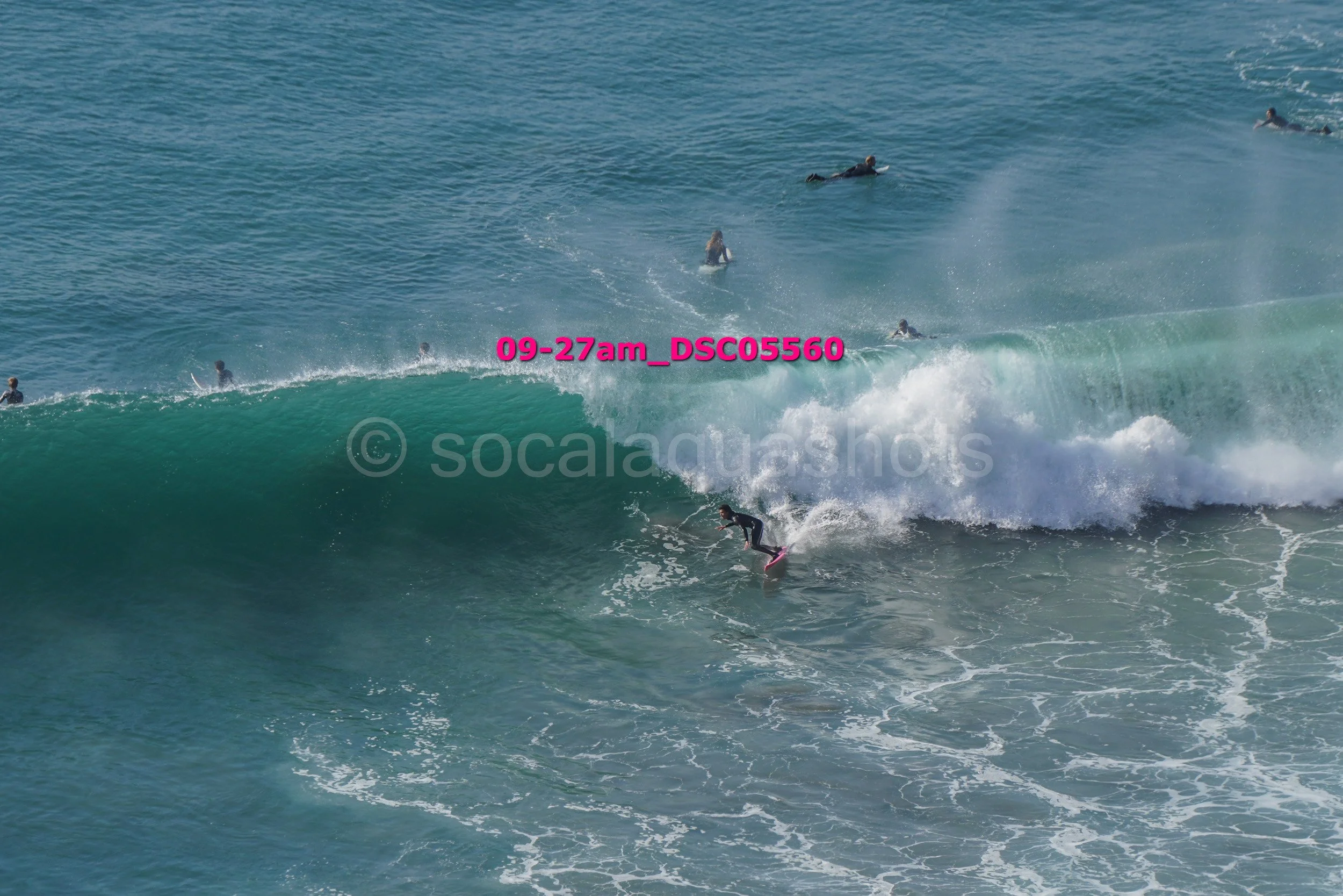 Surfer riding a large wave with several people swimming and surfing in the background in the ocean.