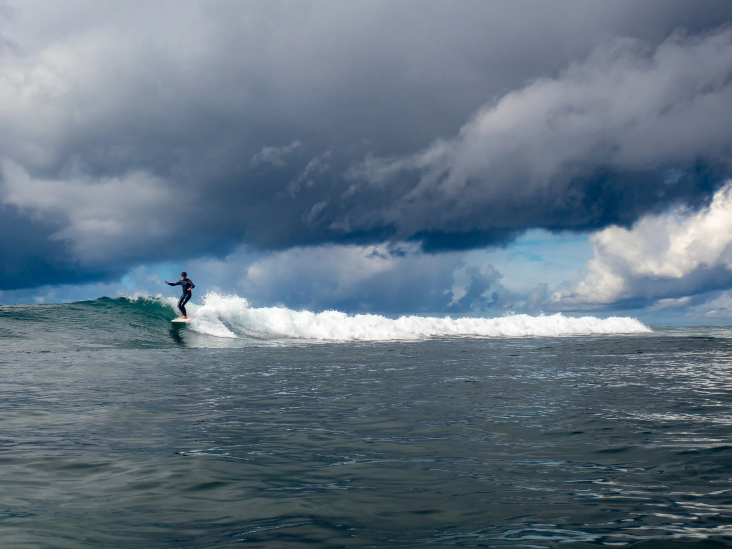 A surfer riding a wave in the ocean under a dark, cloudy sky.