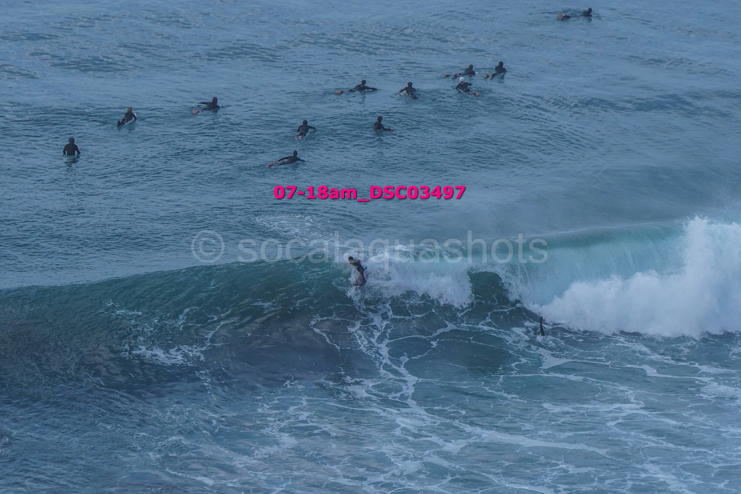 A person surfing a wave in the ocean while a group of people swim and surf in the background.