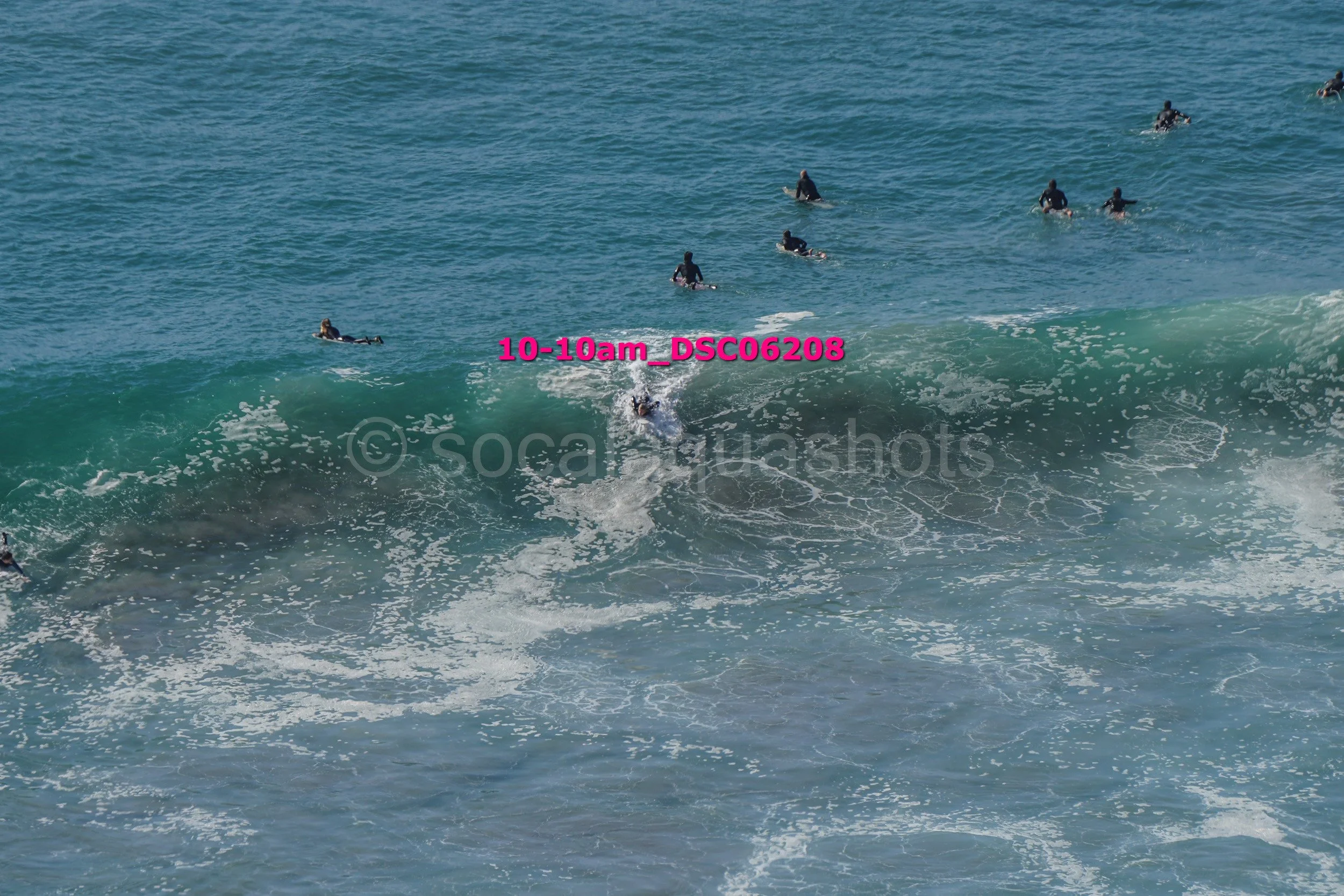 Surfer riding a wave with several surfers in the water watching, in the ocean during daytime.