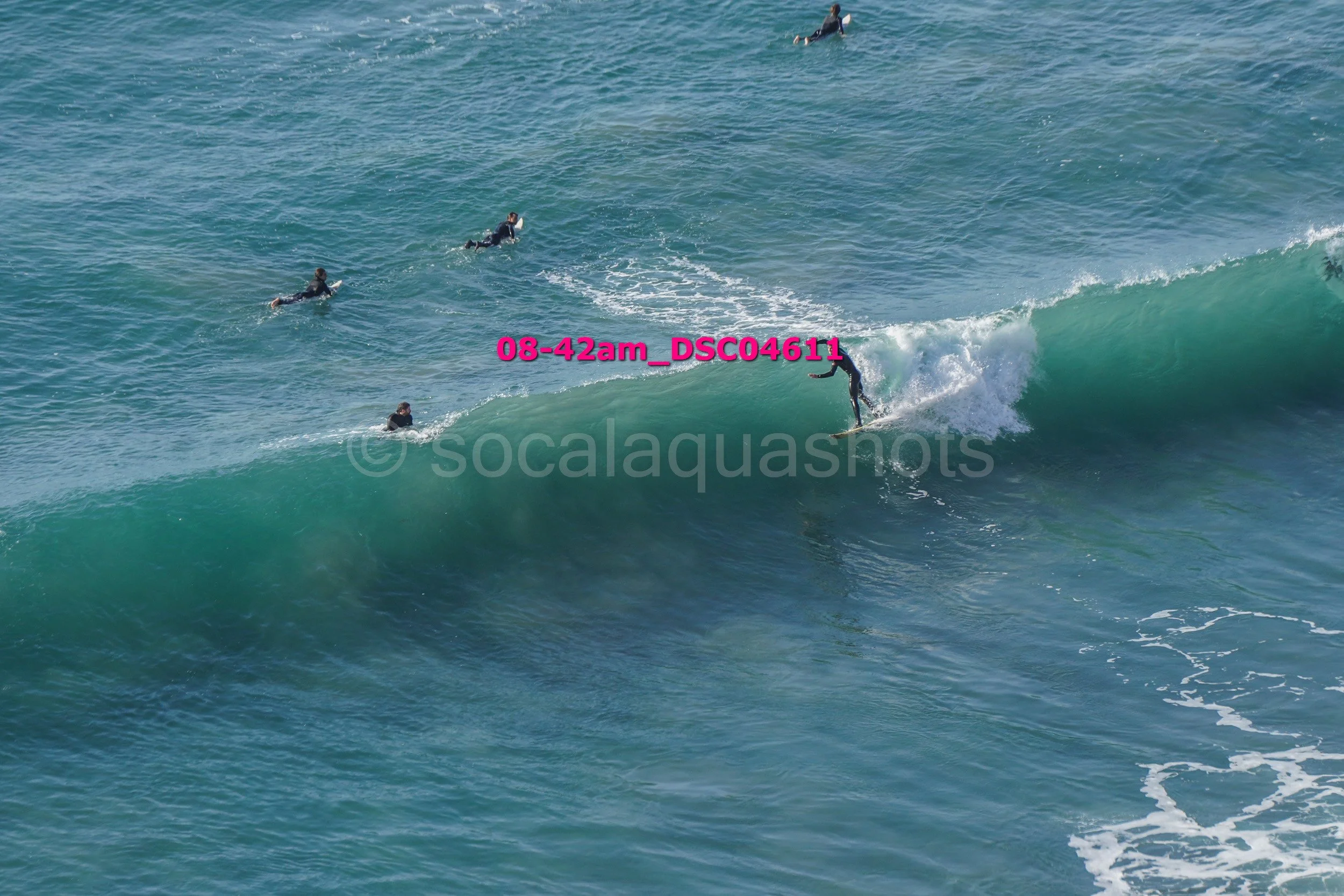 A surfer riding a wave with several other surfers in the water watching nearby.
