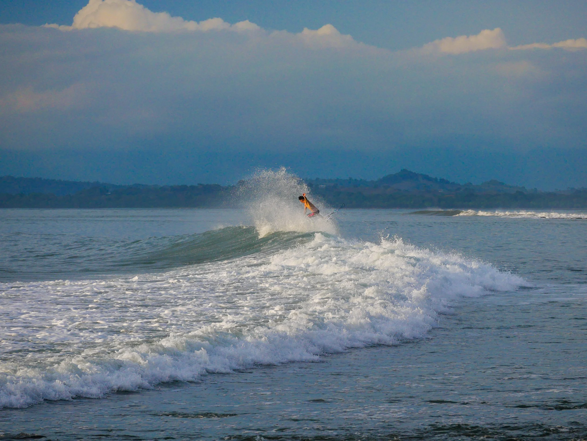 Surfer riding a wave in the ocean with mountains in the background.