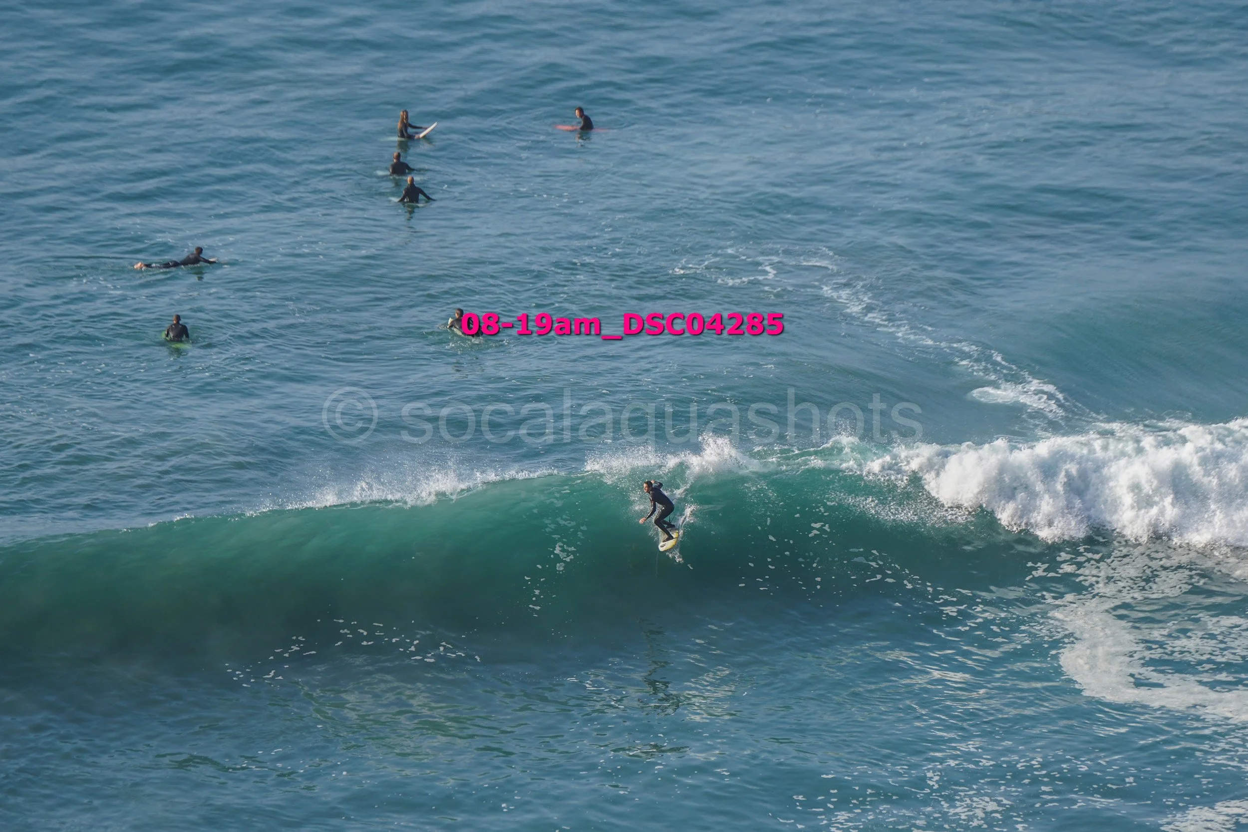 A person surfing on a wave with several people swimming and watching from the water in the background.