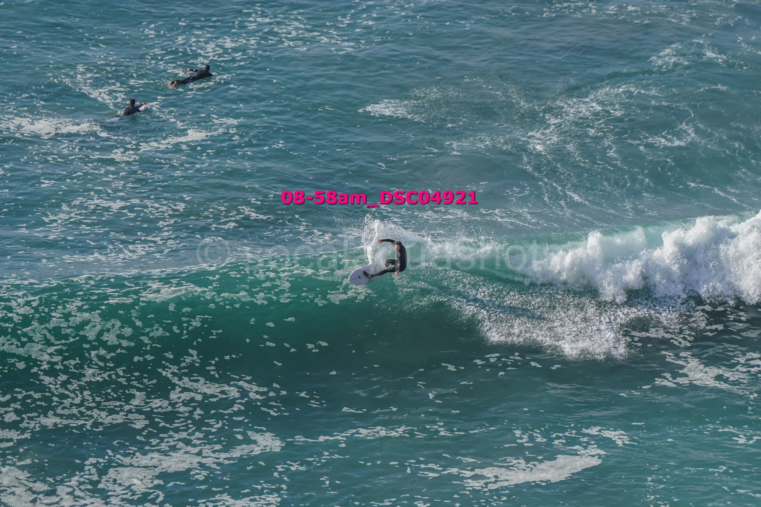 Surfer performing a trick on a wave in the ocean, with two other surfers visible in the water nearby.