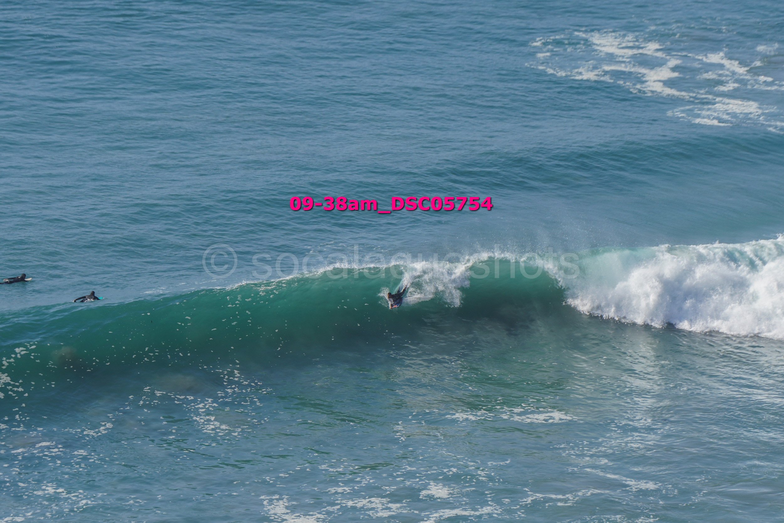 Surfer riding a wave in the ocean with two other surfers in the water nearby.