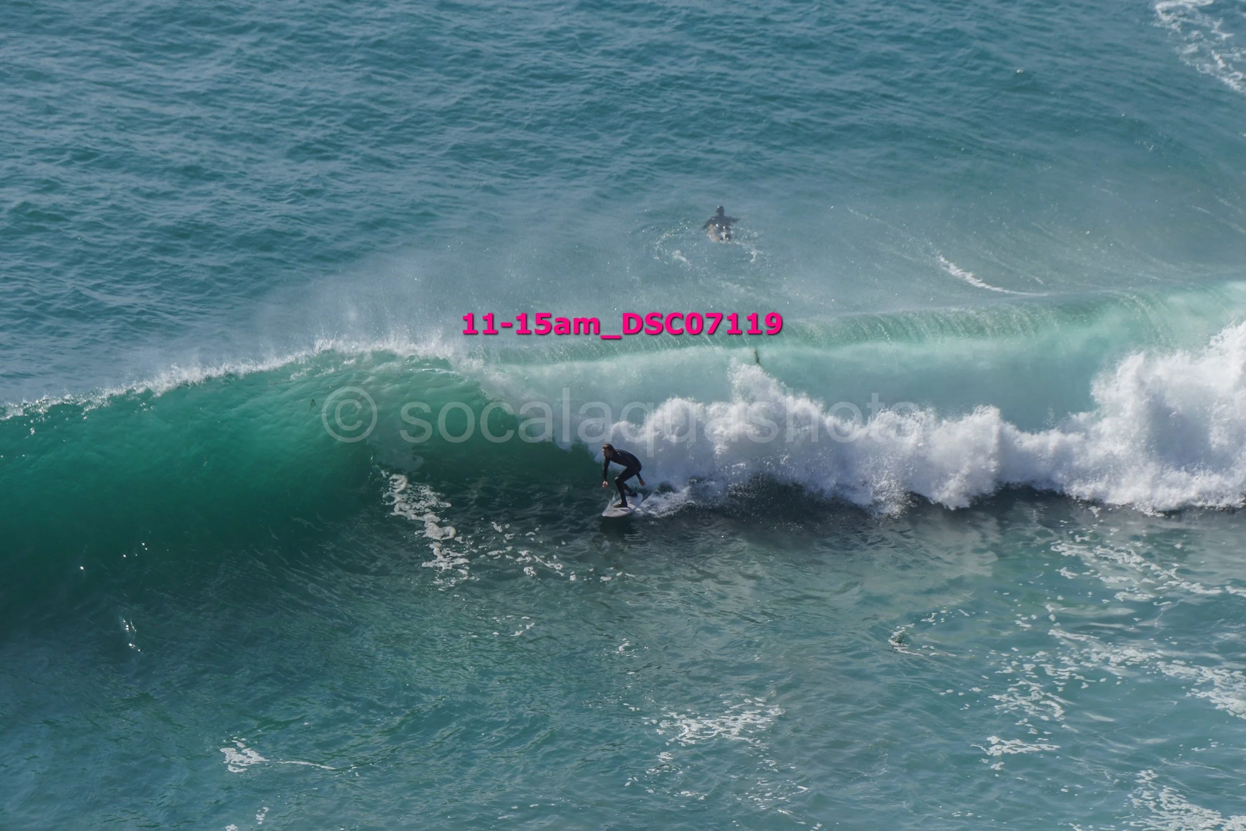 A surfer rides a wave in the ocean with another surfer visible in the distance.