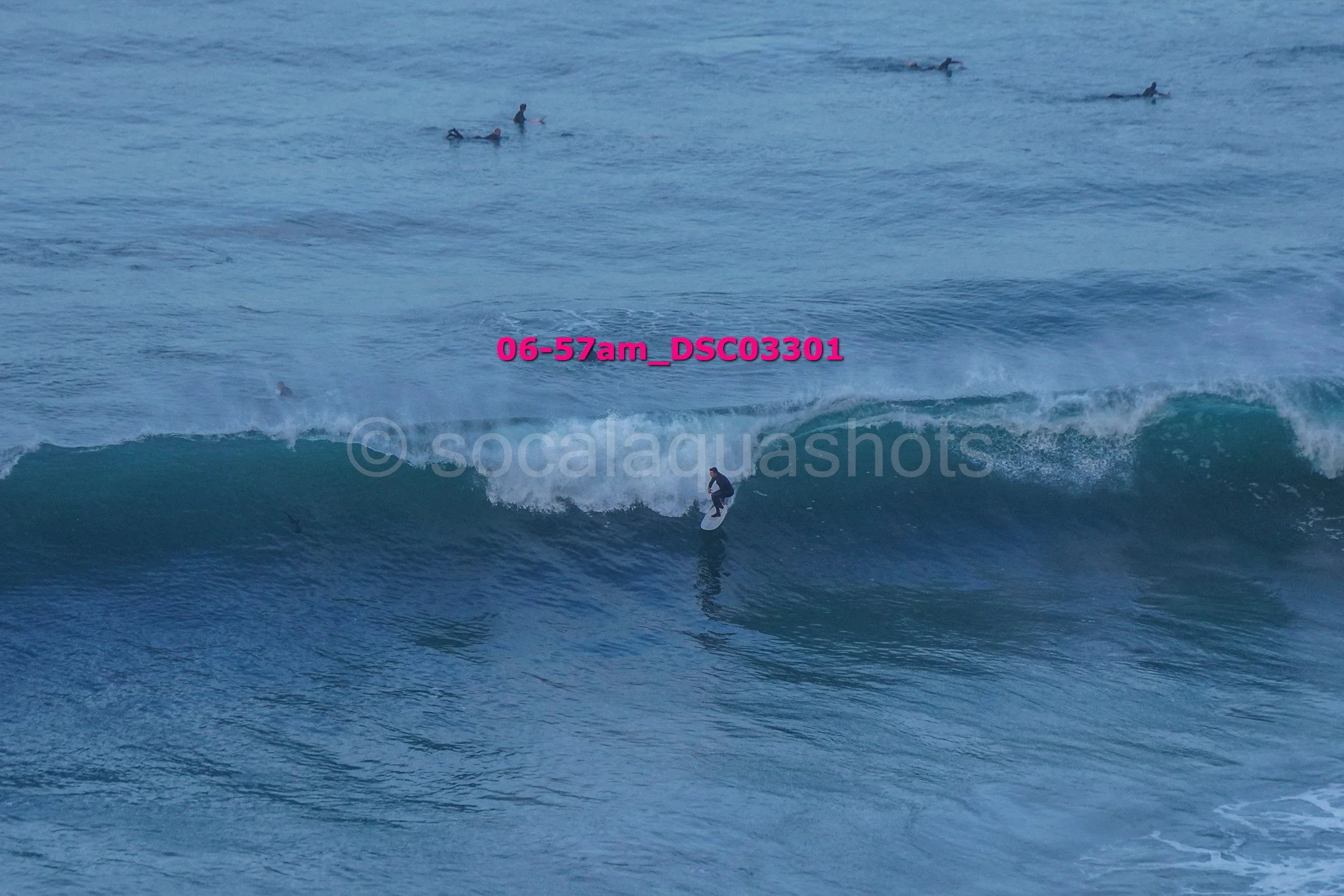 A person surfing on a wave in the ocean with several other surfers in the background.