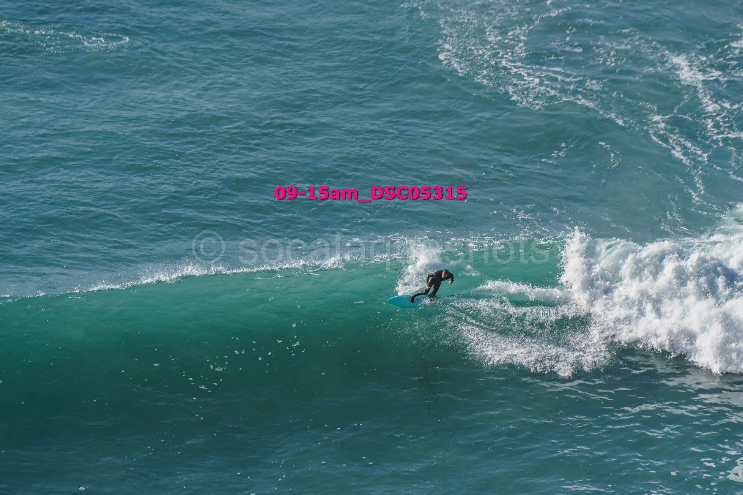 A person surfing on a blue surfboard riding a wave in the ocean, with water splashing around.