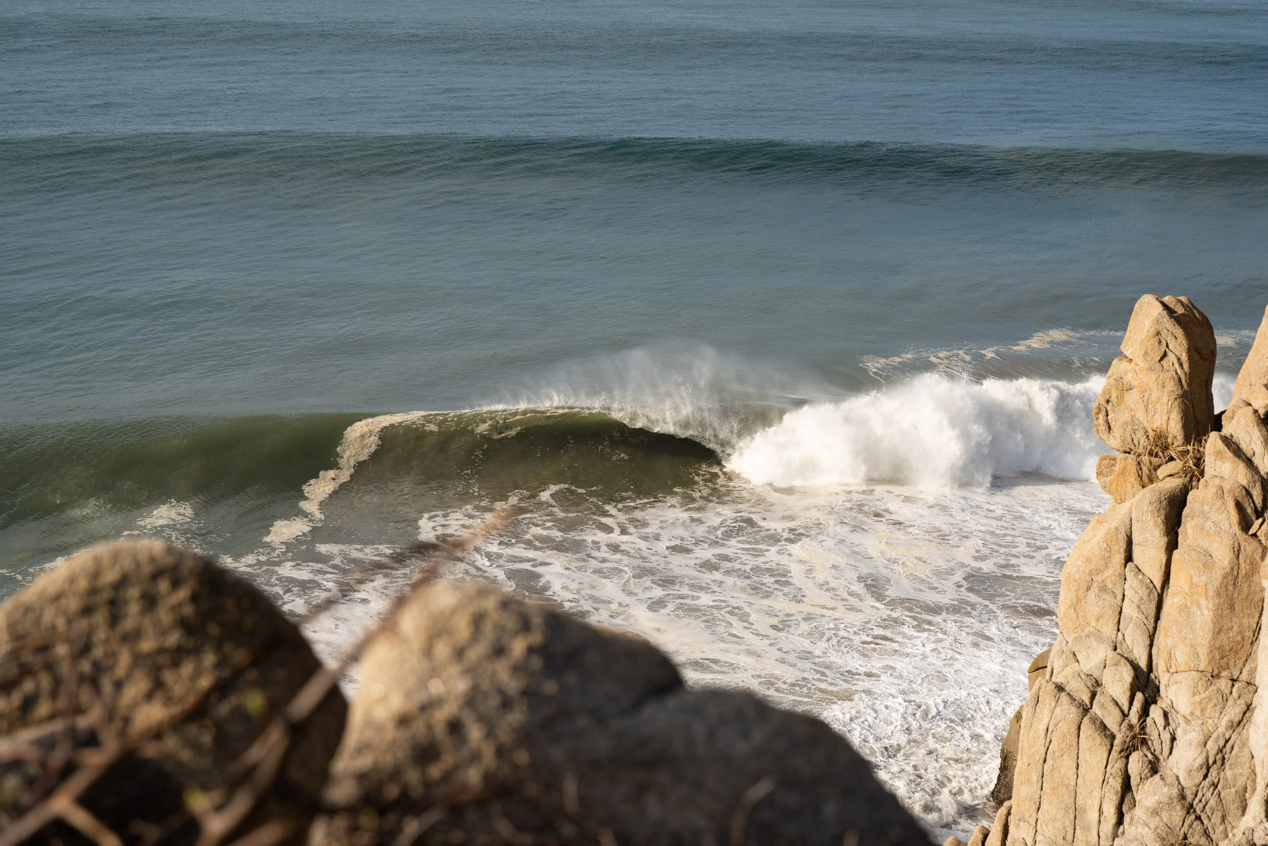 View of ocean waves breaking on the shore with rocks in the foreground.