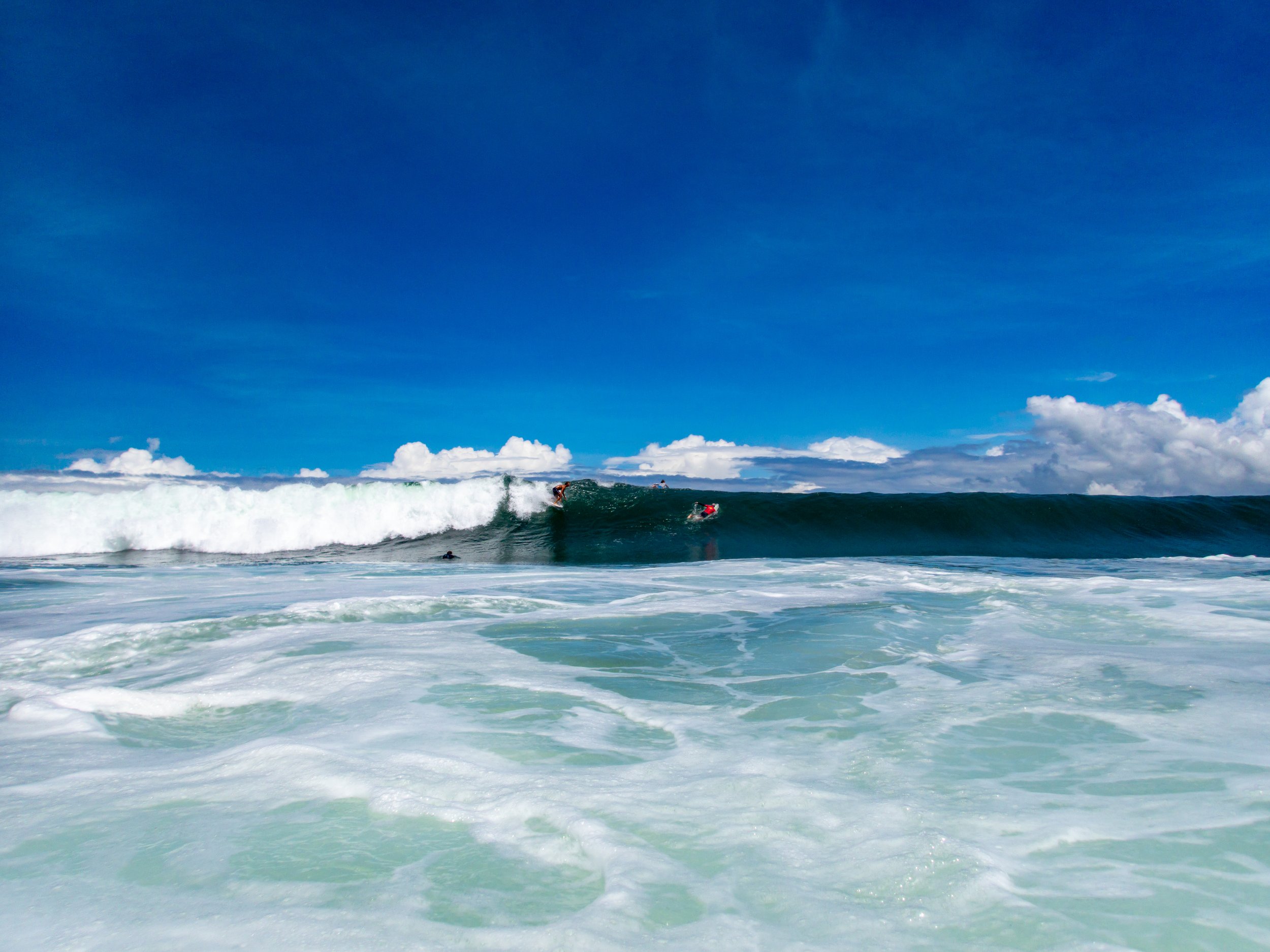 surfer riding a large ocean wave under a clear blue sky