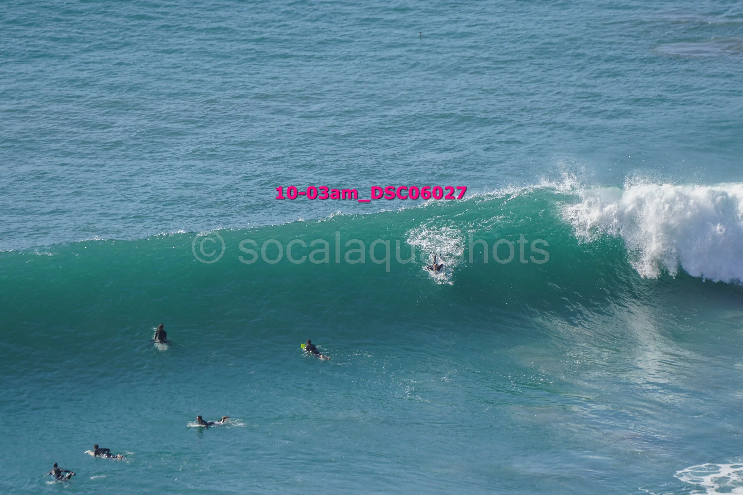 Several surfers in the ocean, with one riding a large wave.