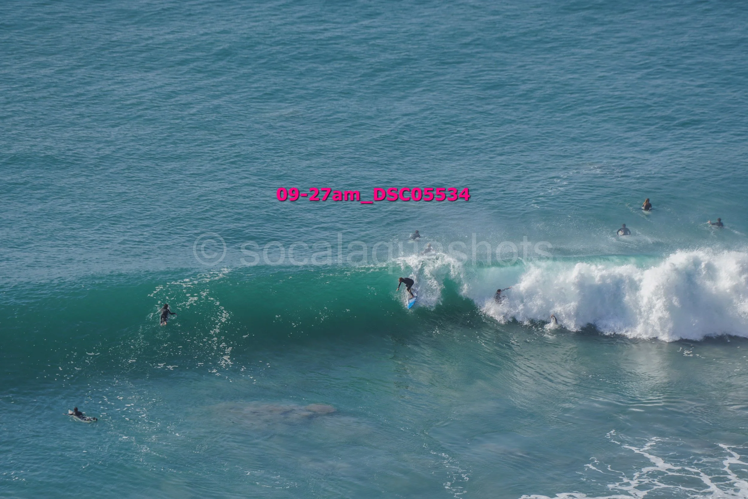 A group of surfers riding and swimming in the ocean waves on a sunny day.